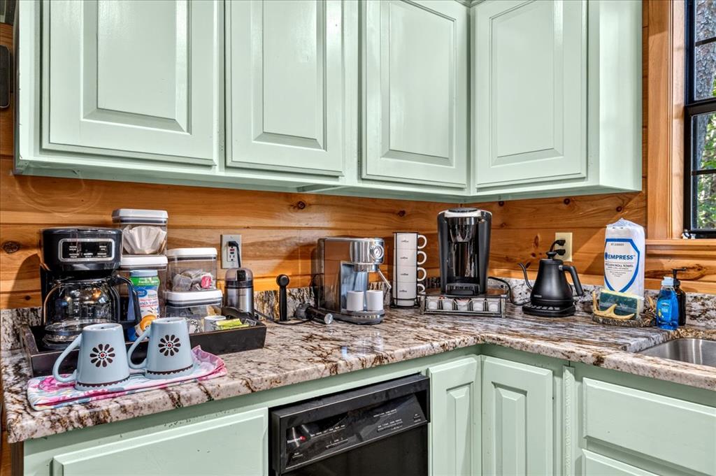 Kitchen coffee station with pale green cabinets, granite counters, and a wood backsplash.
