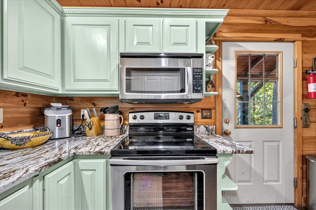 Kitchen with mint-green cabinets, granite counters, stainless-steel appliances, and warm wood-plank walls.