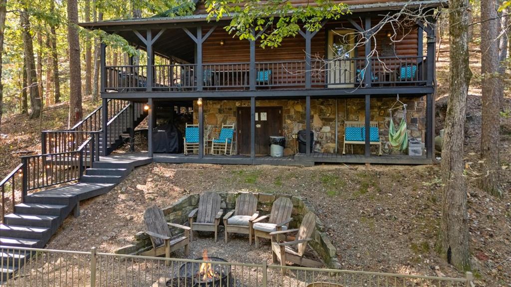 Wooded cabin with a covered upper deck, exterior stairs, and a fire pit seating area.