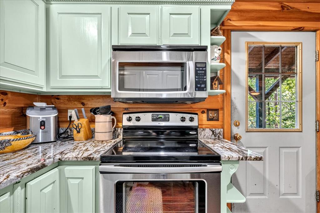 Kitchen with mint-green cabinets, stainless steel appliances, marble-pattern counters, and a wood-plank backsplash.