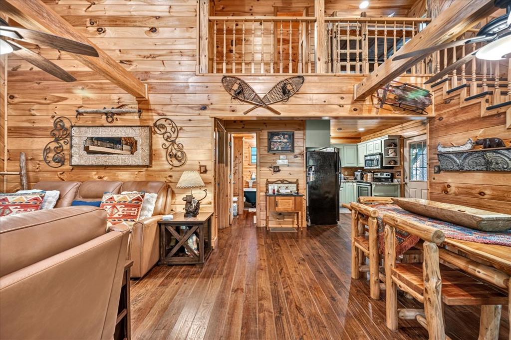 Open-plan wood cabin living room and kitchen with a loft, leather seating, and rustic furniture.