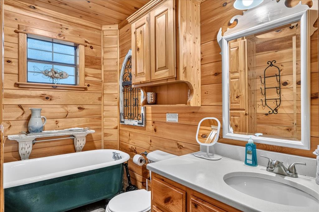 Wood-paneled bathroom with a green clawfoot tub and wood vanity beneath an ornate mirror.