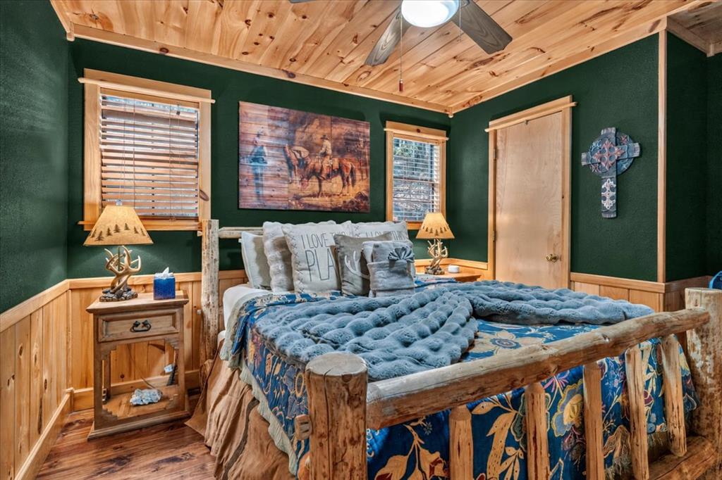 Furnished bedroom with a rustic log bed, blue patterned bedding, and dark green walls beneath a wood ceiling.