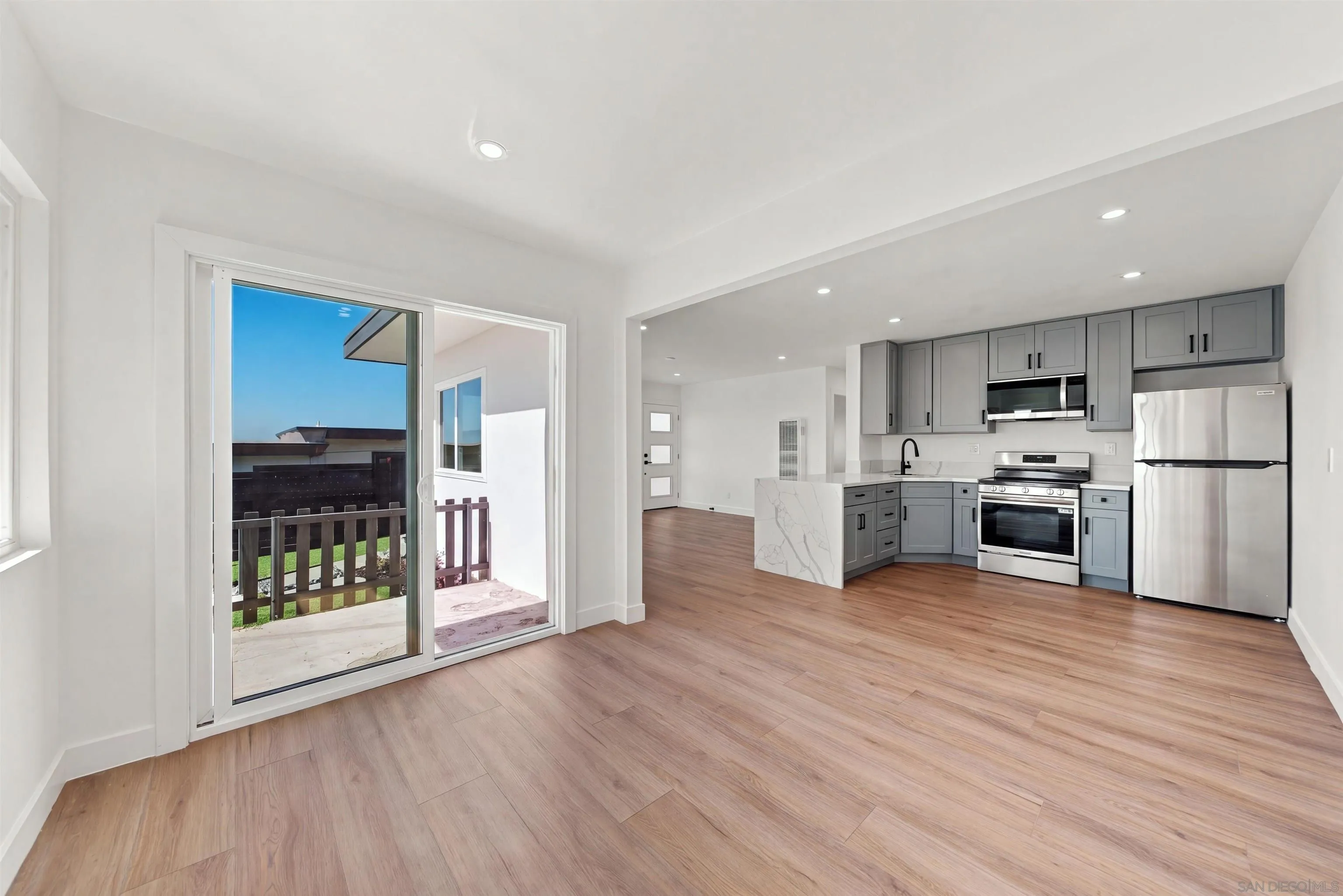 Vacant kitchen with gray cabinets and stainless appliances beside a sliding glass door to a patio.