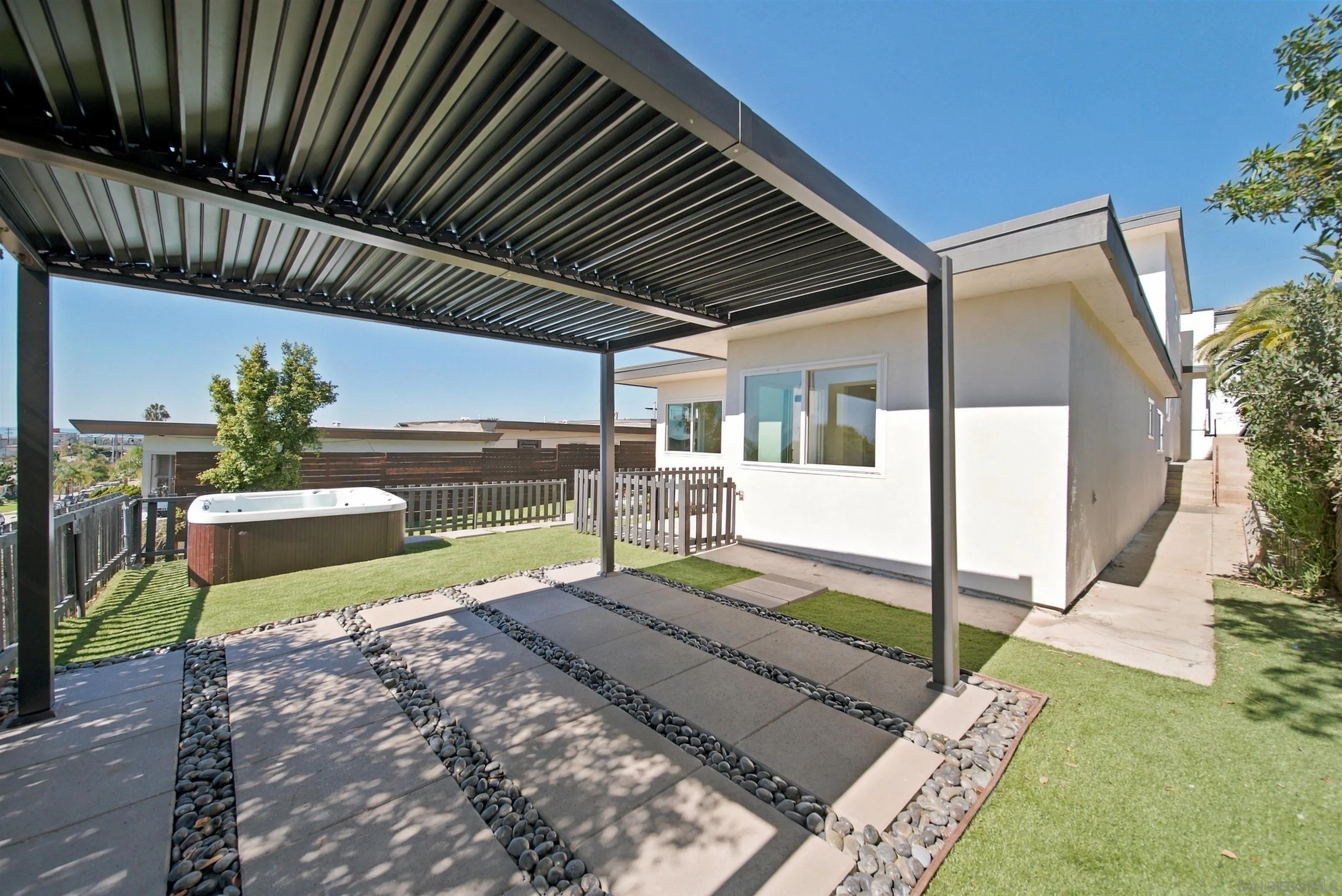 Modern home patio with a louvered pergola, paved walkway, artificial turf, and fenced hot tub.