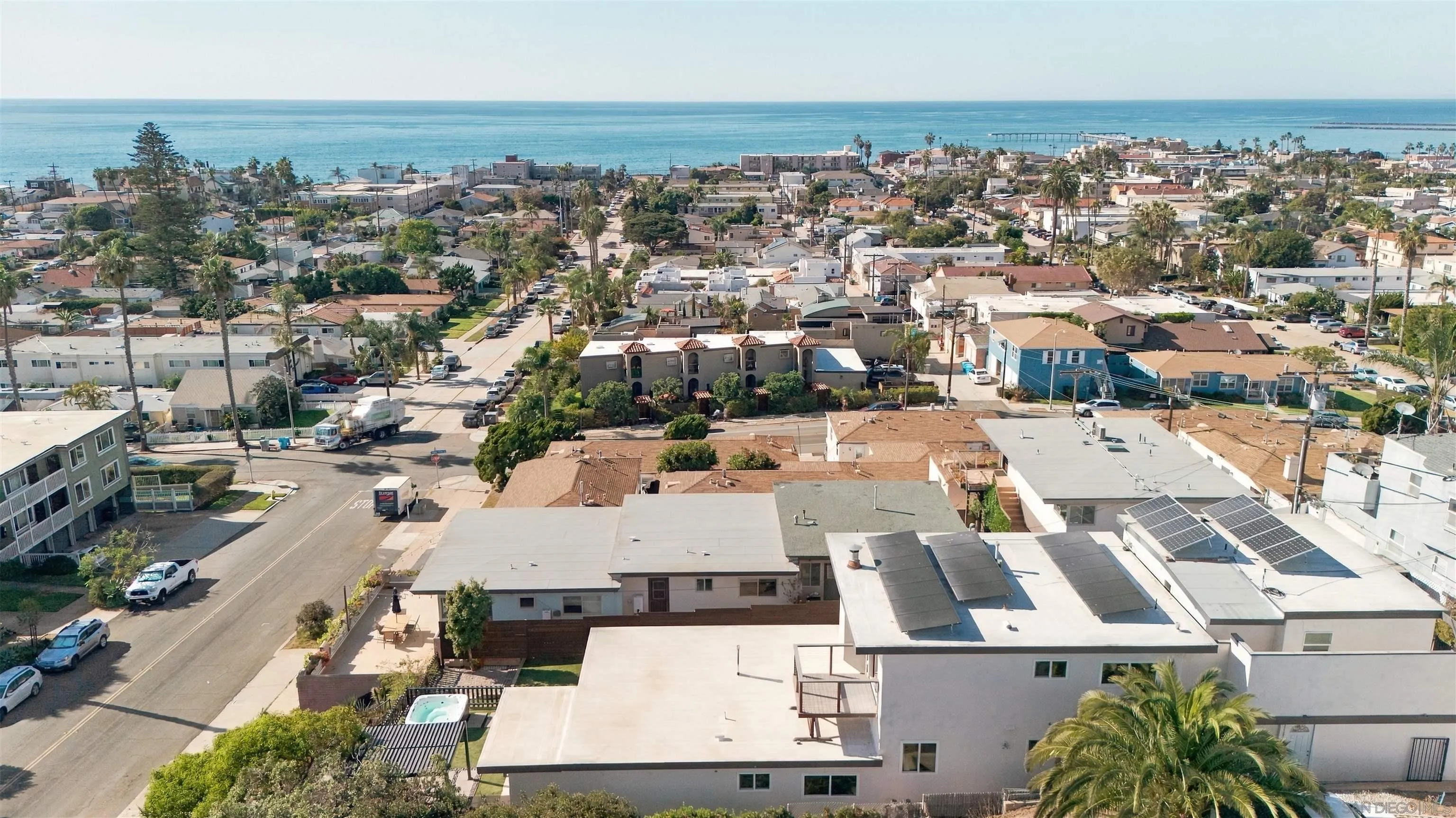 Aerial view of a coastal neighborhood, with the ocean beyond solar-panel rooftops.