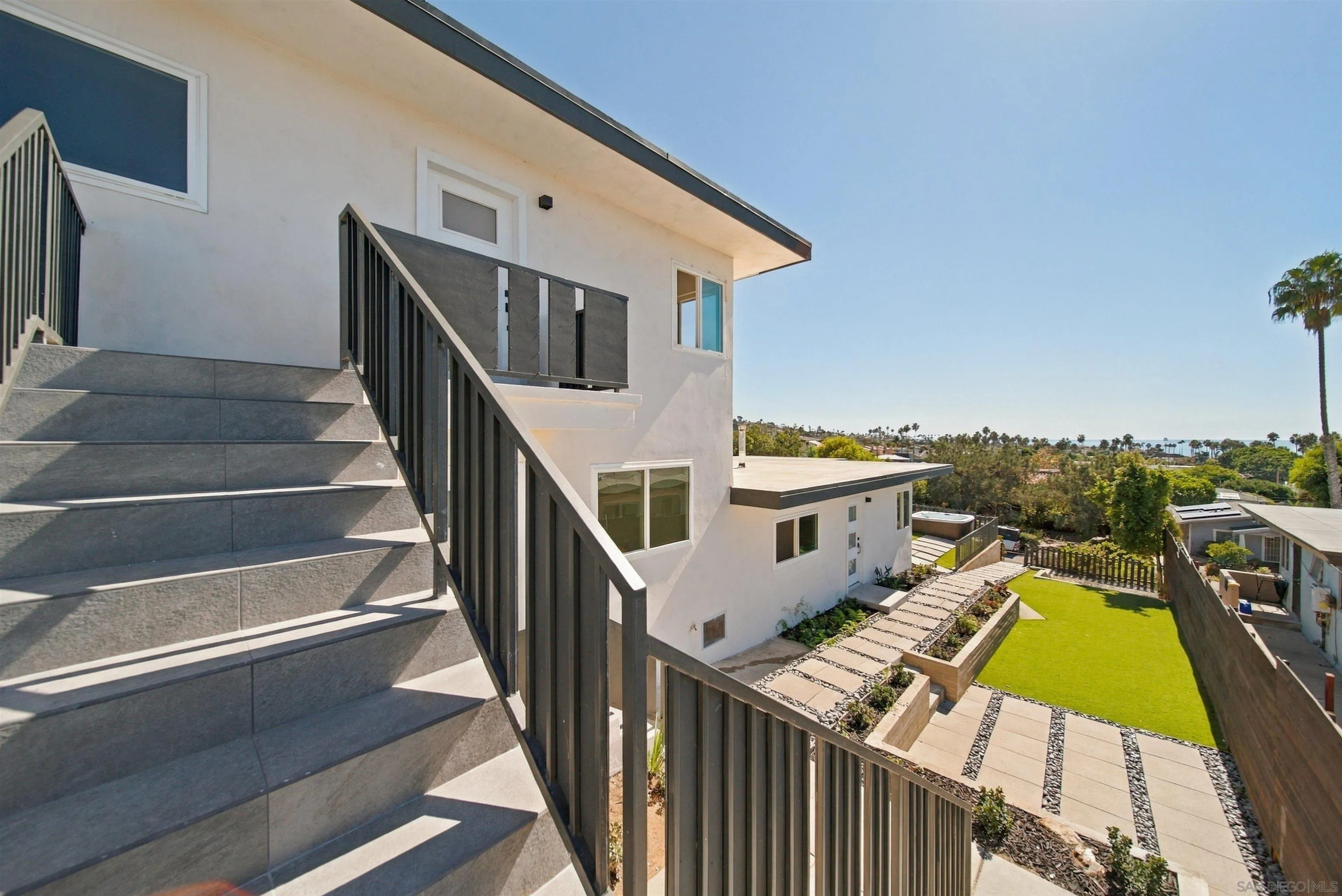 Modern white home with a broad exterior staircase overlooking a landscaped lawn and distant ocean.
