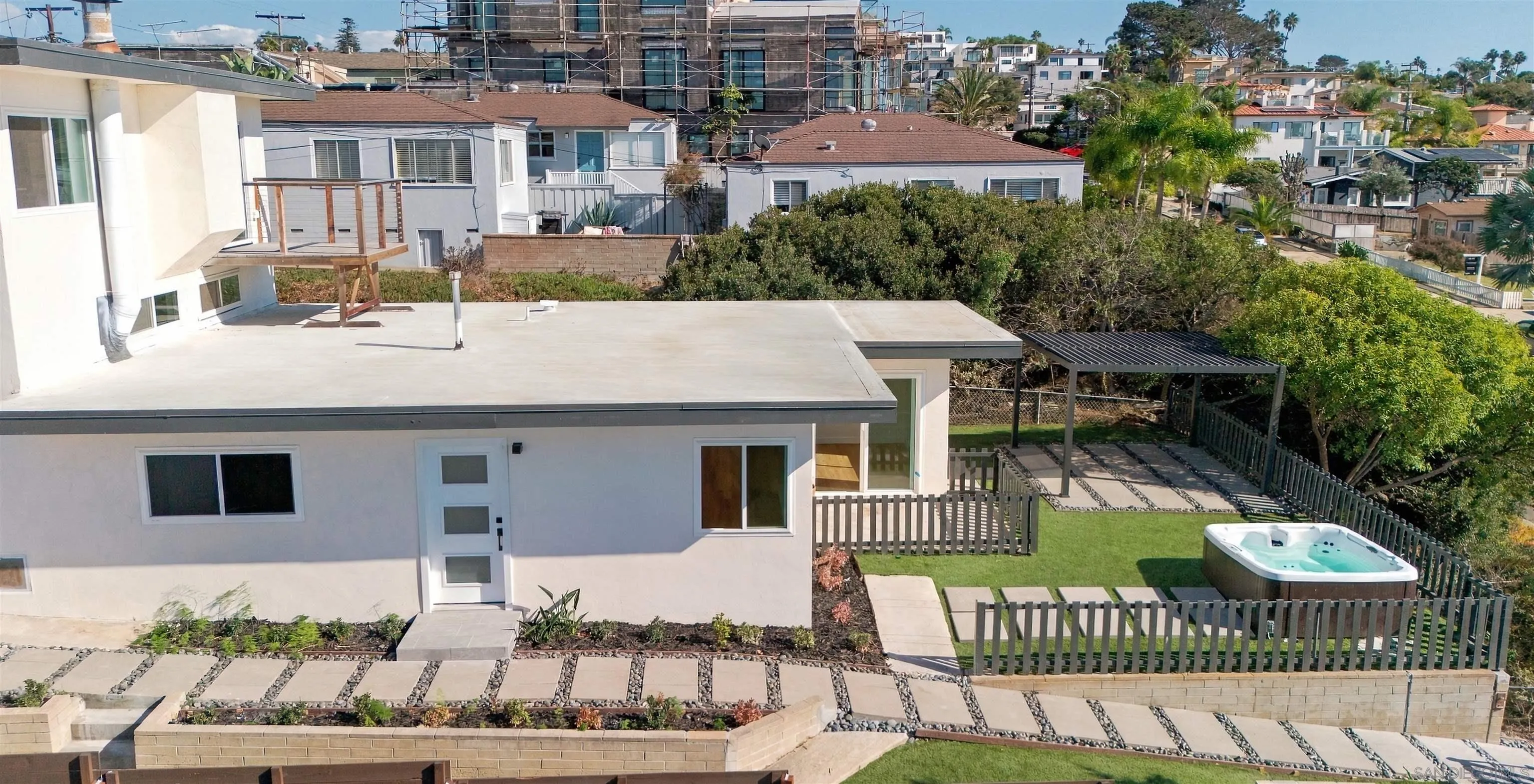 Elevated view of a modern white home with a fenced lawn, pergola, and backyard hot tub.