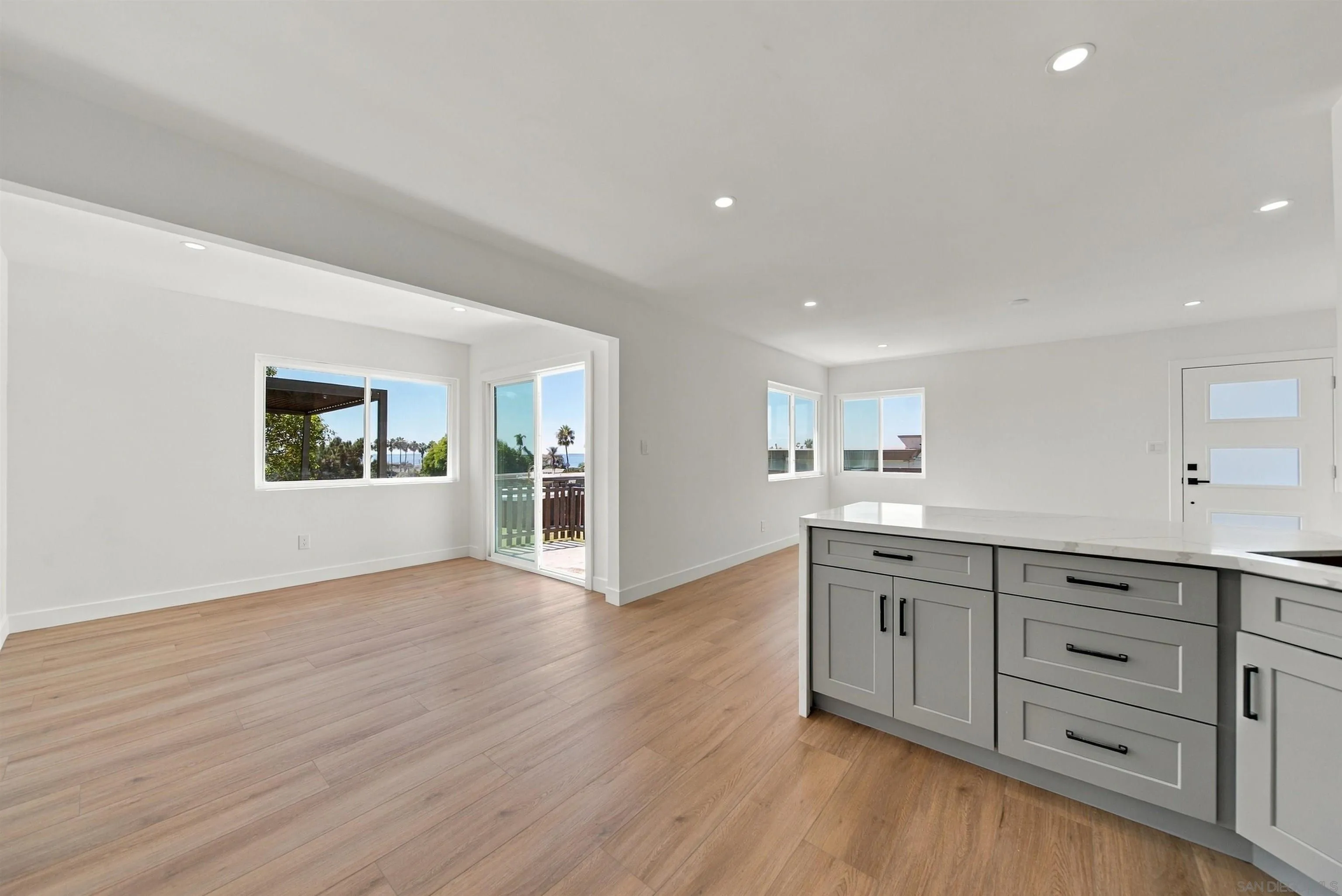 Open-plan kitchen and living area with a gray island, wood floors, and ocean glimpses through the windows.
