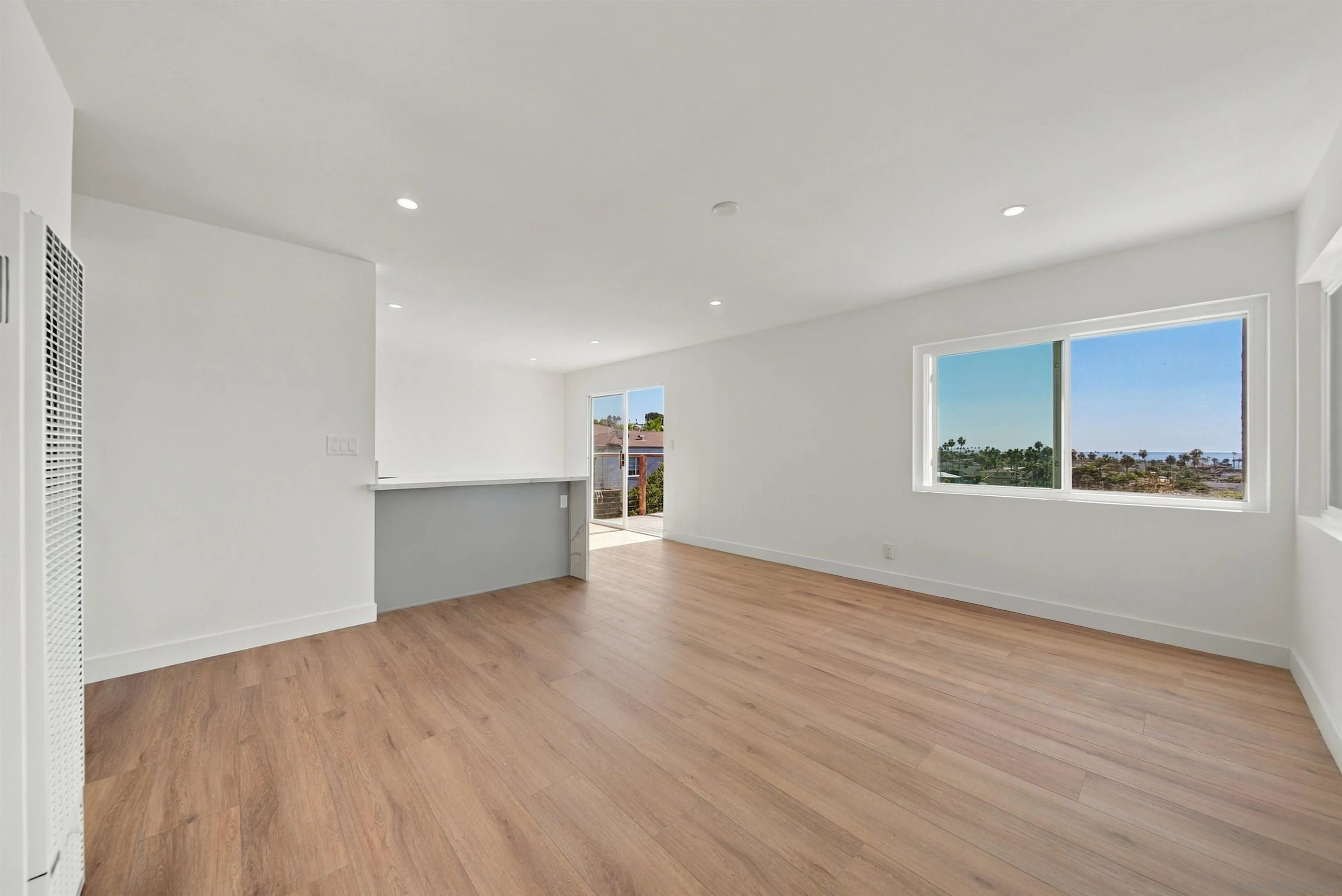 Vacant living area with wood floors, a breakfast bar, and an ocean view through the large window.