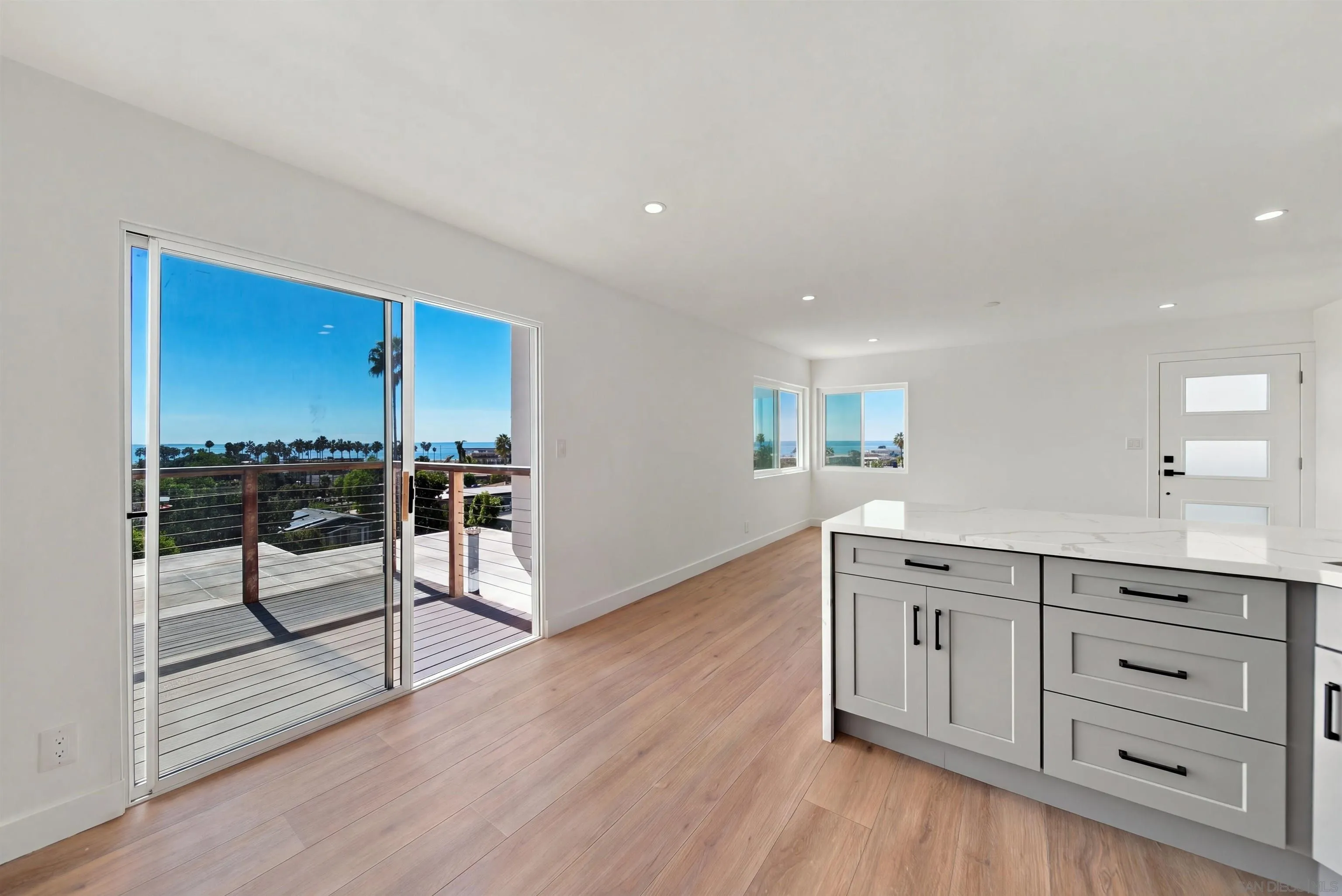 Bright kitchen with a white island, wood floors, and ocean views through sliding glass doors.