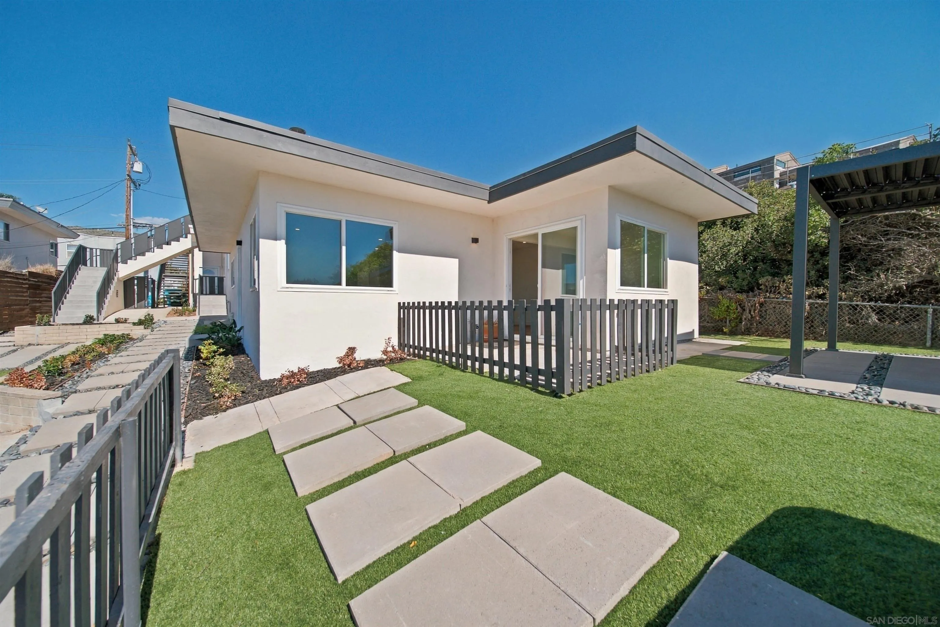 Modern white home with a fenced patio, artificial lawn, and concrete stepping stones.