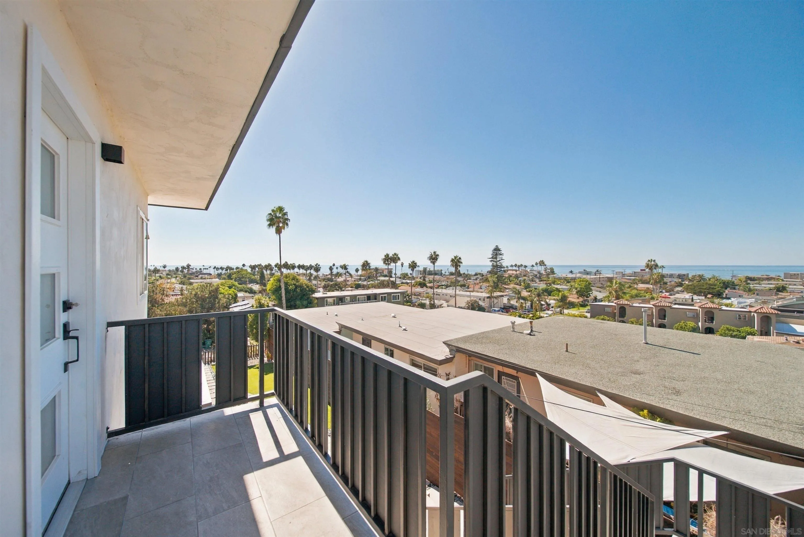 Balcony overlooking a coastal neighborhood and the ocean, with palm trees along the horizon.