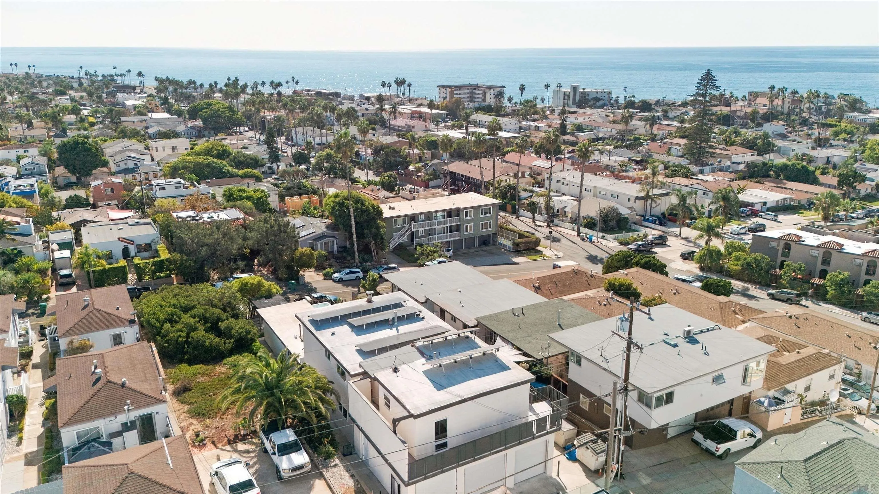 Aerial view of a multi-unit property near the coast, with surrounding homes and ocean beyond.