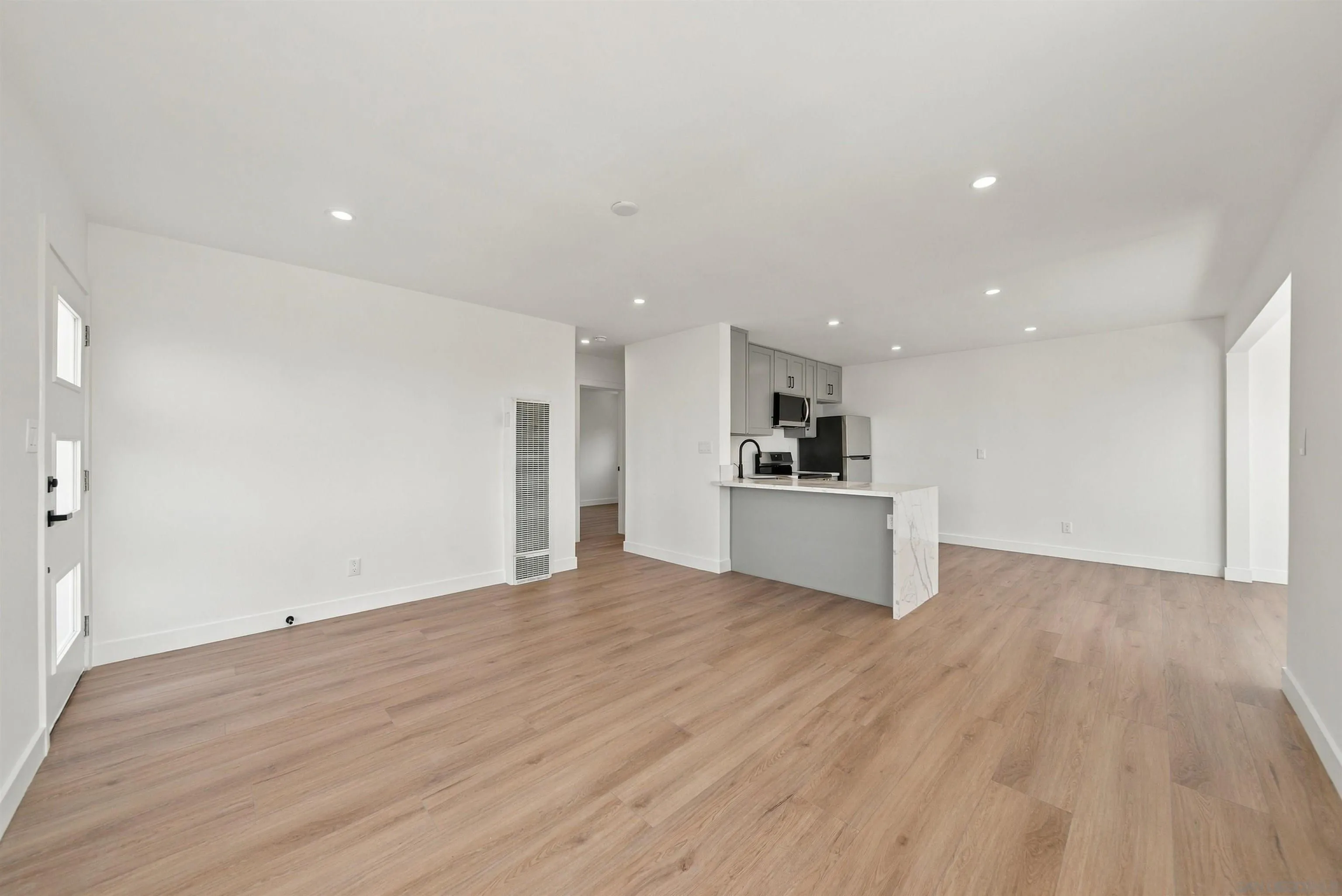 Open-plan living area with wood flooring and a compact kitchen with a gray peninsula.
