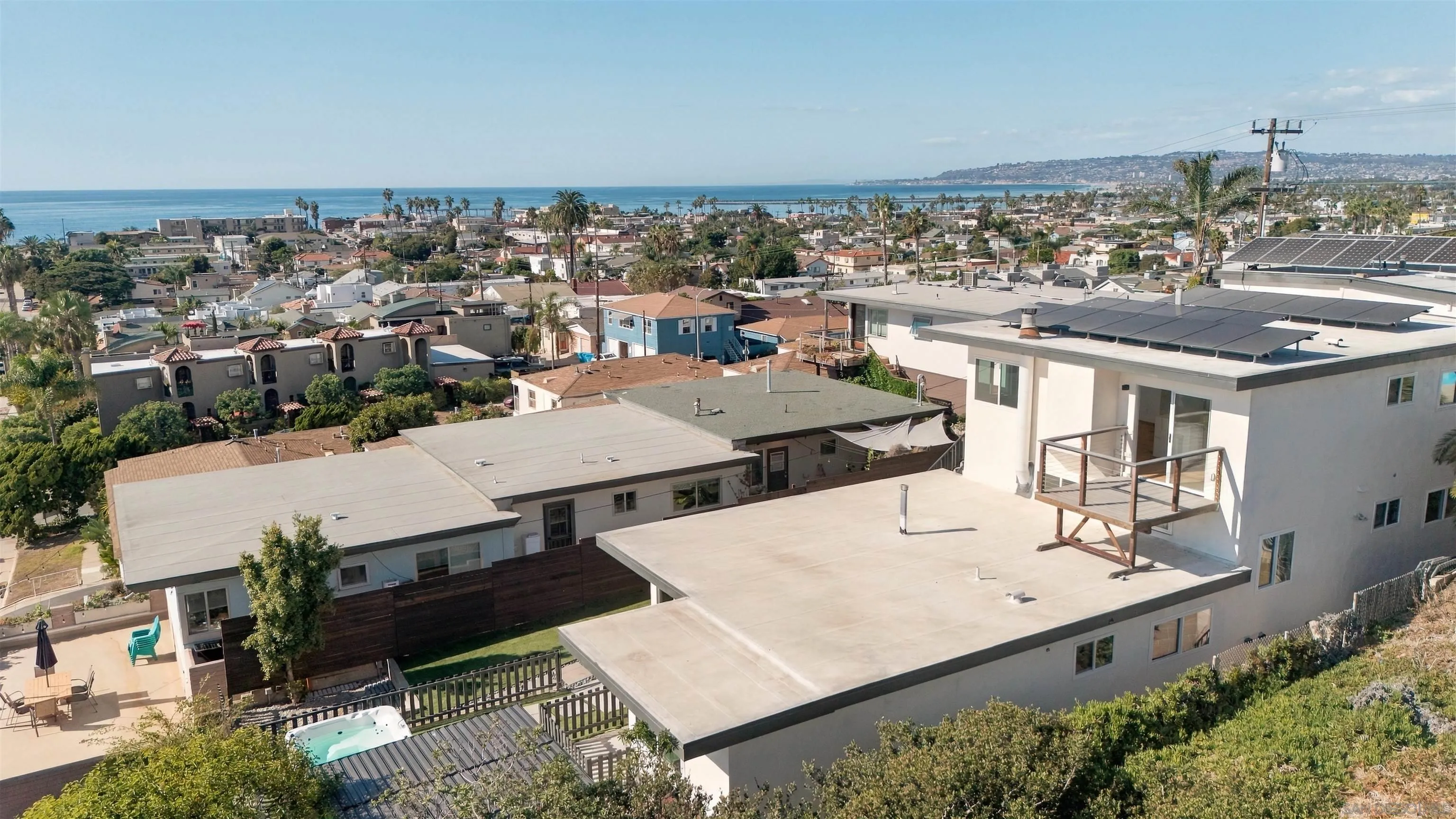 Modern coastal home with rooftop solar panels and hot tub, overlooking the Pacific Ocean.