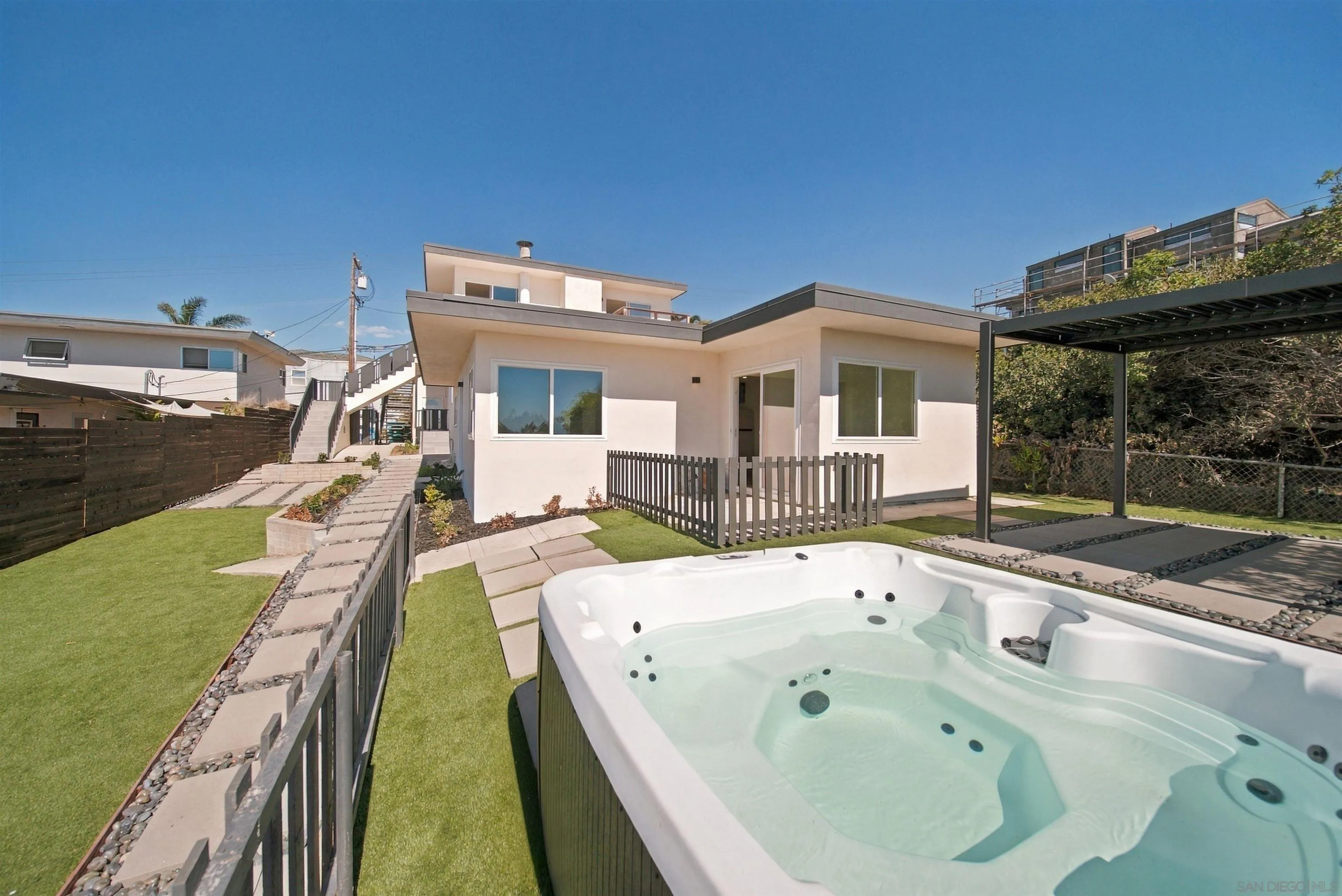 Modern home exterior with a large hot tub, fenced lawn, and covered patio.