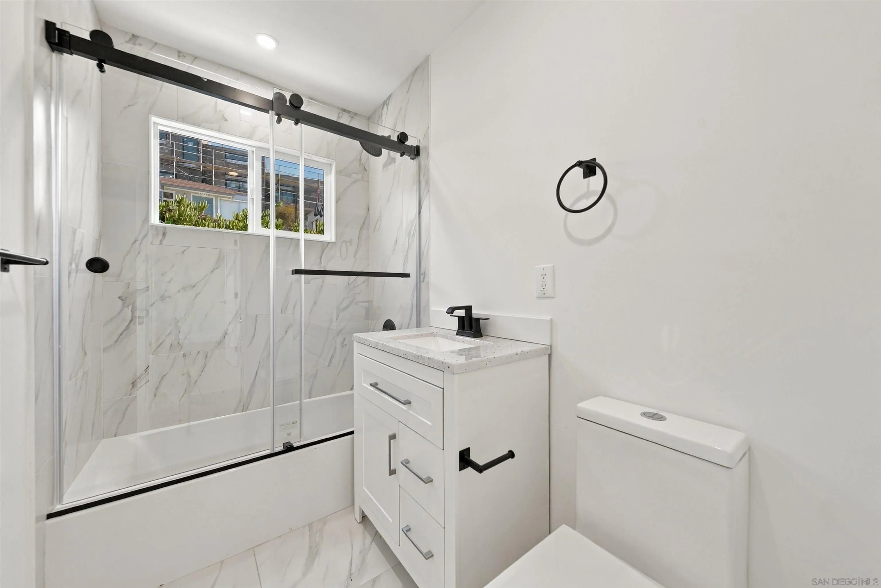 Renovated bathroom with a marble-look tiled shower, glass doors, white vanity, and black fixtures.