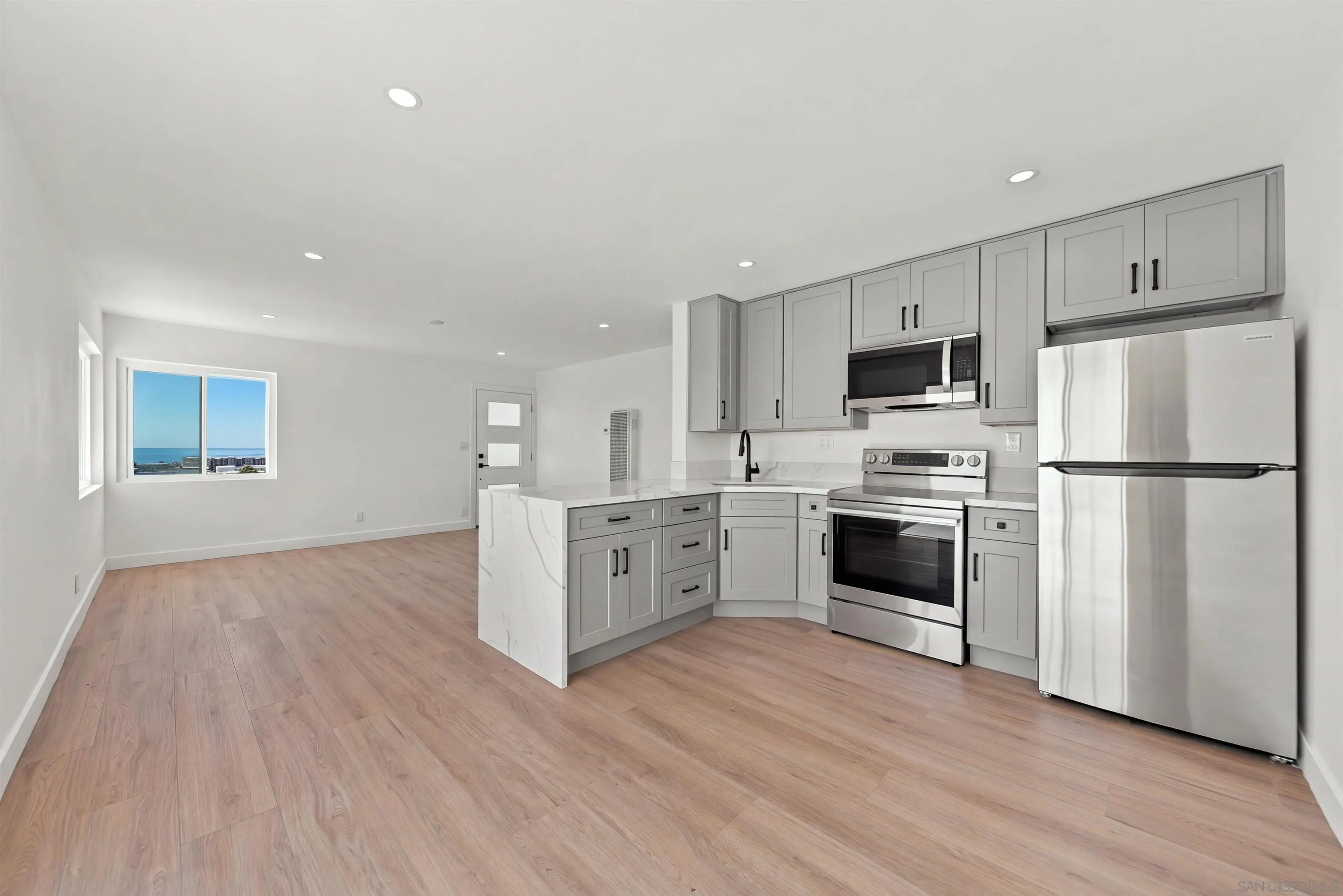 Vacant kitchen with gray cabinets, stainless steel appliances, and an ocean view through the window.