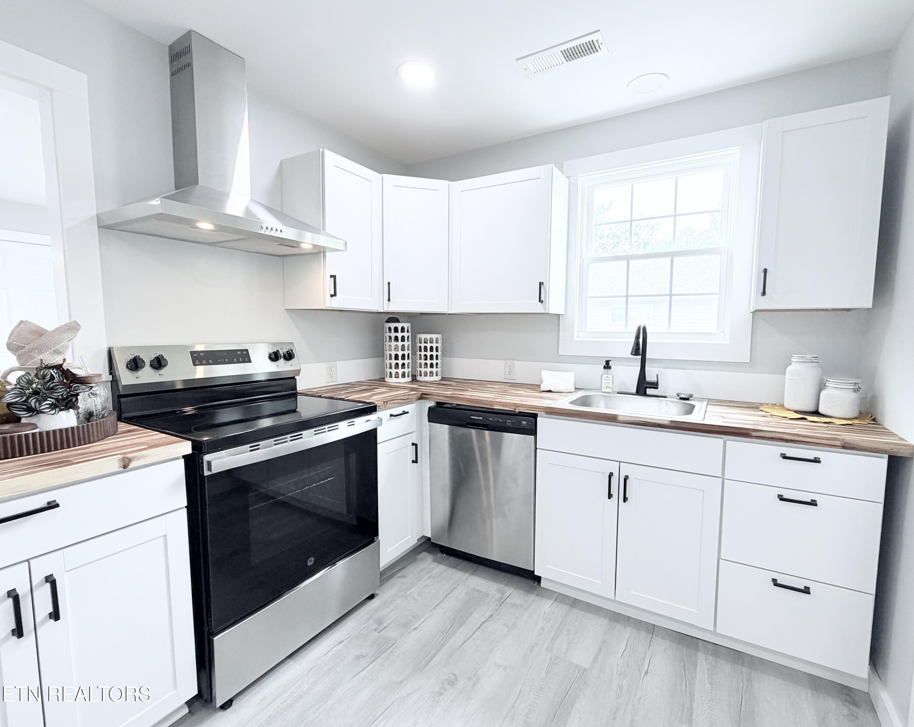 Bright kitchen with white cabinets, striped wood countertops, a black range, and stainless steel hood.