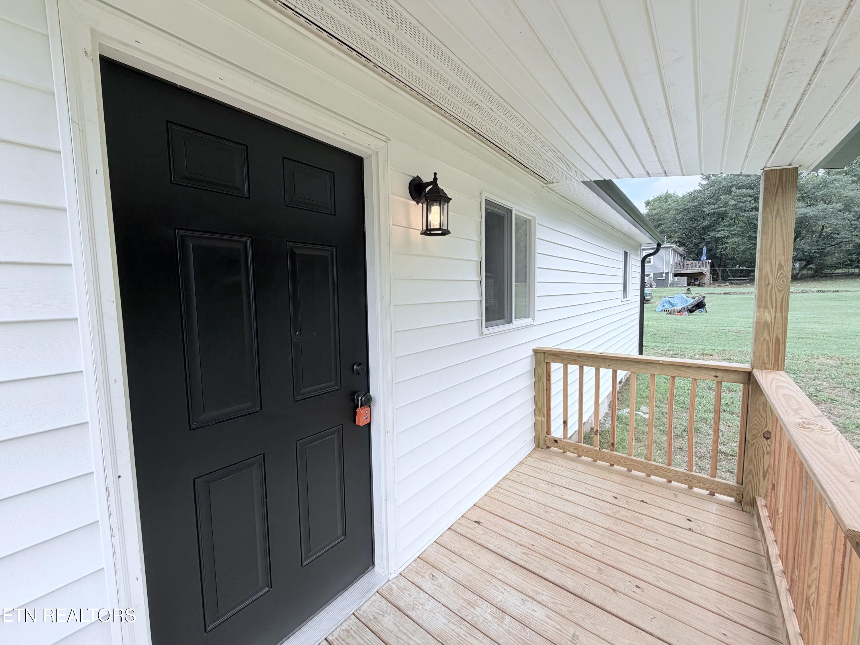Covered front porch with a black entry door, white siding, and new wooden decking.