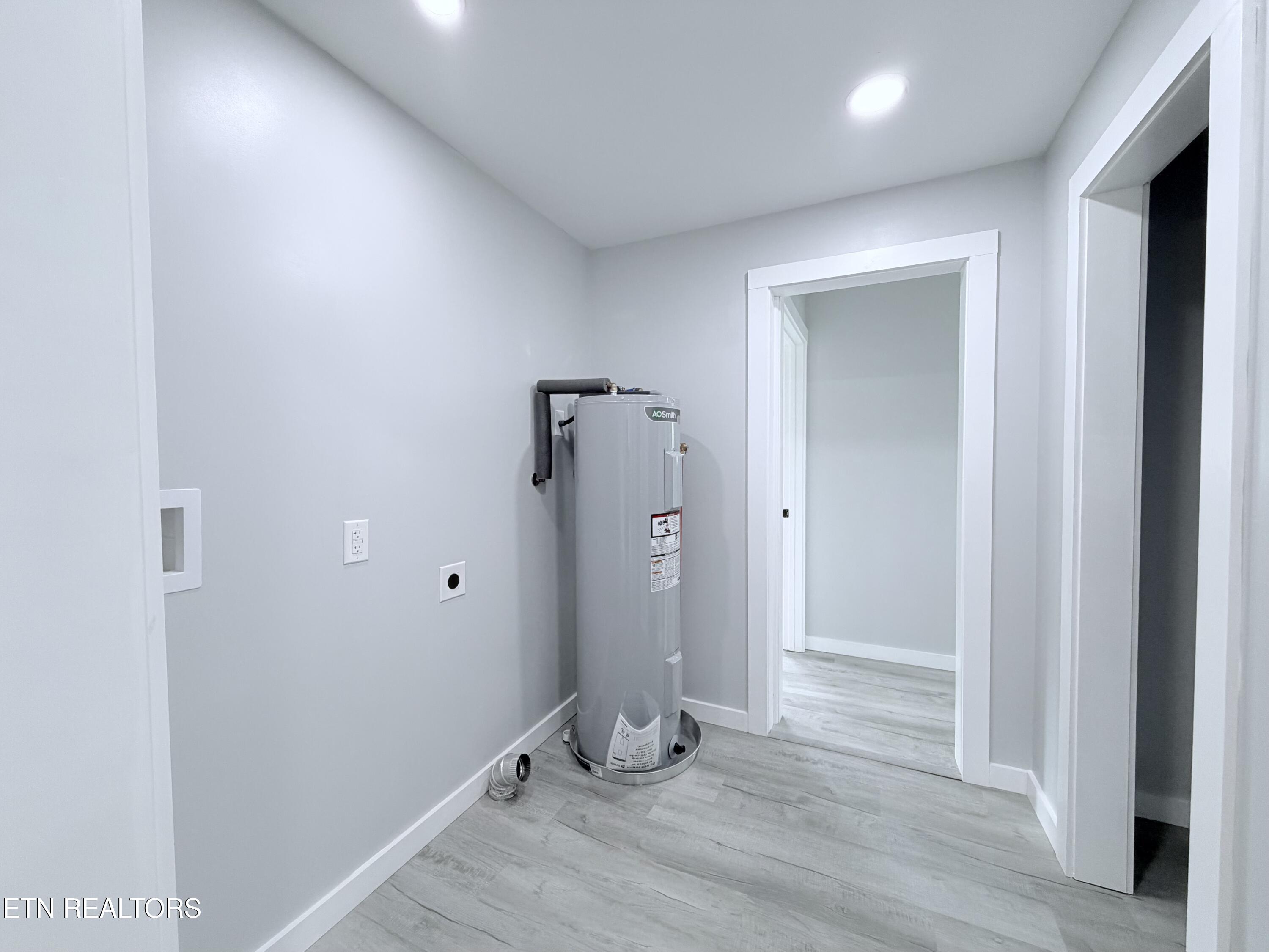 Utility room with a tall water heater, gray plank flooring, and doorways to adjoining rooms.