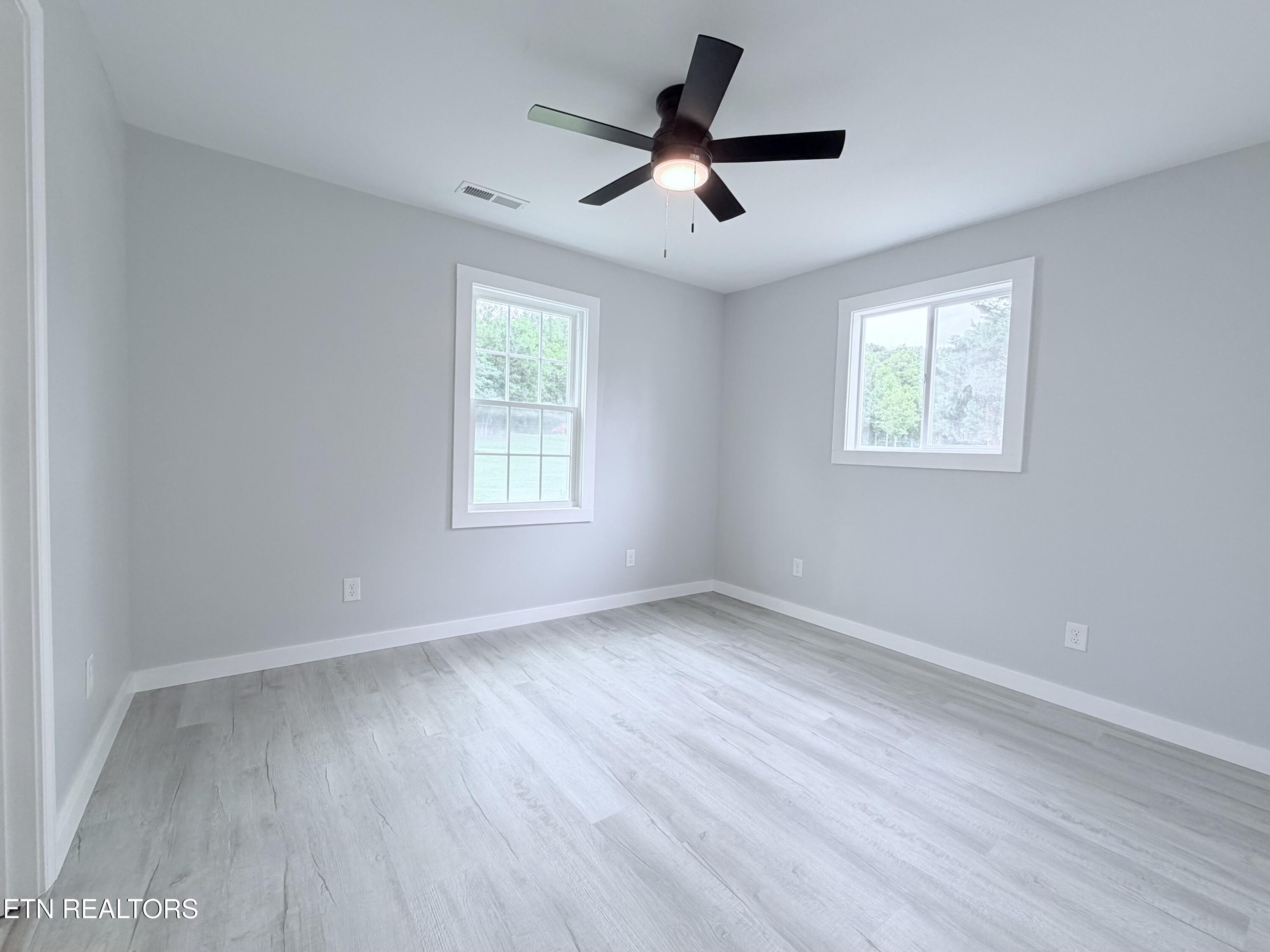 Empty room with pale wood-look flooring, two windows, and a black ceiling fan.