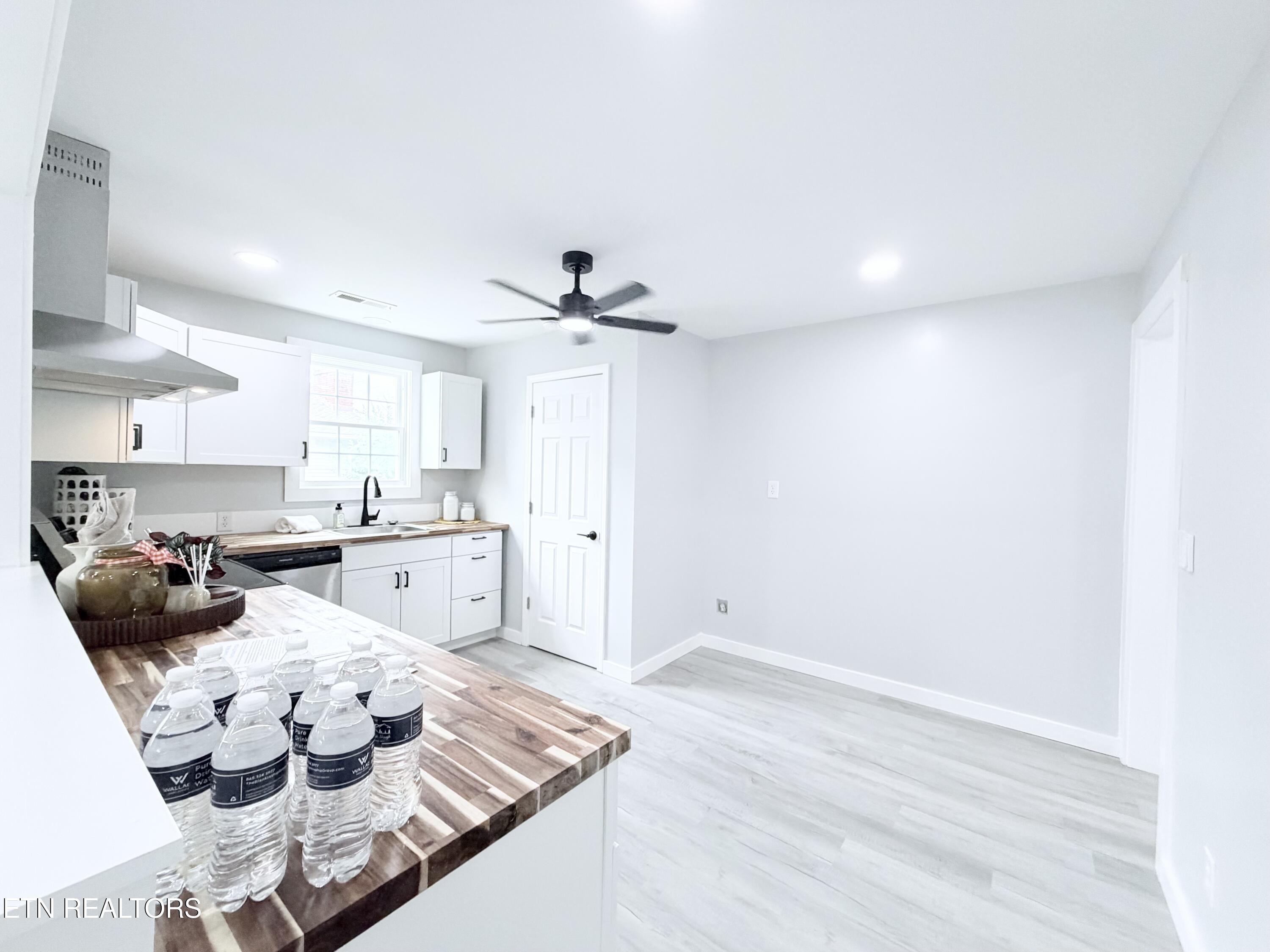 Bright kitchen with white cabinets, butcher-block counters, a black faucet, and ceiling fan.