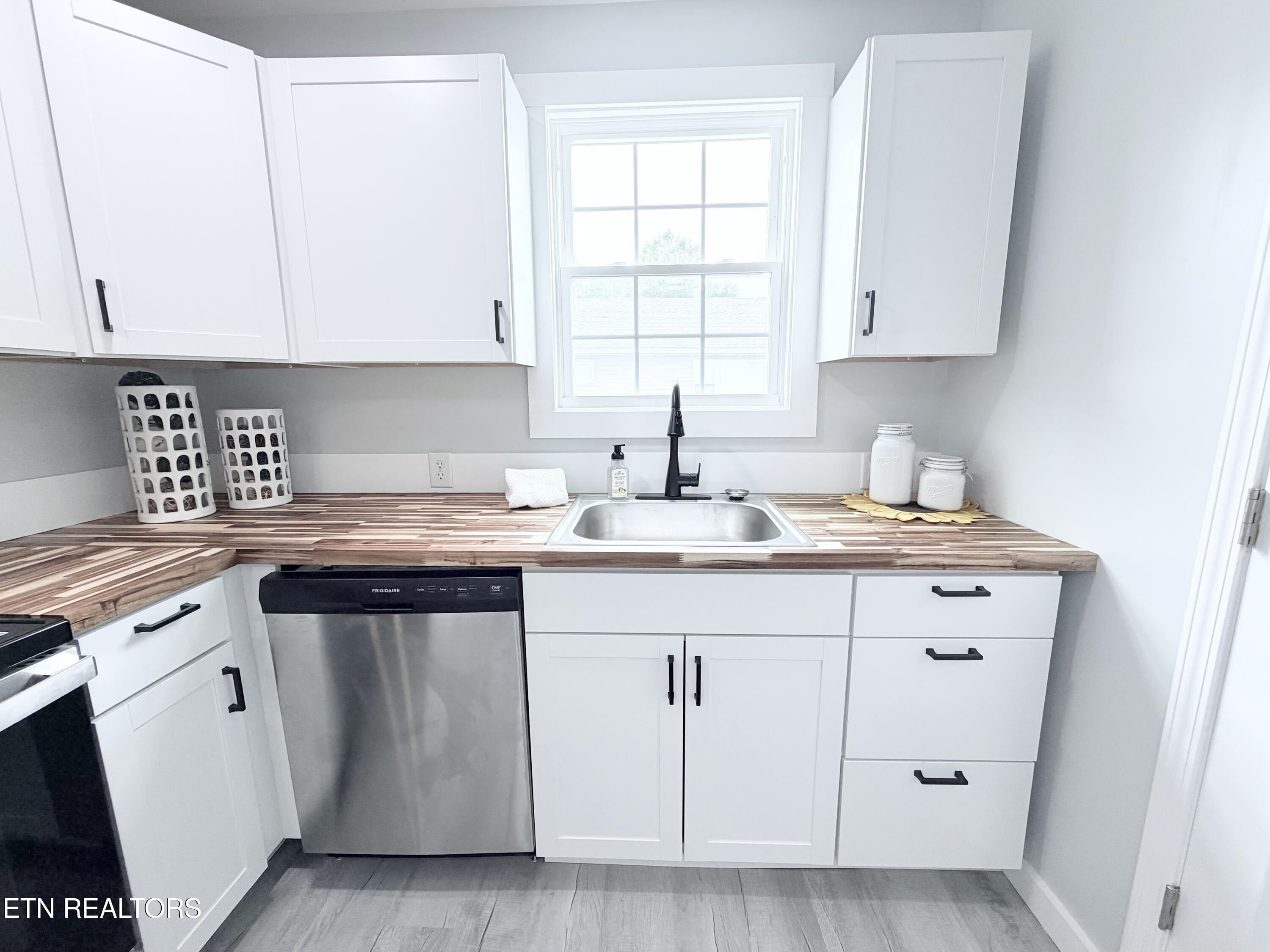 Kitchen with white cabinets, wood-look counters, and a sink beneath the window.