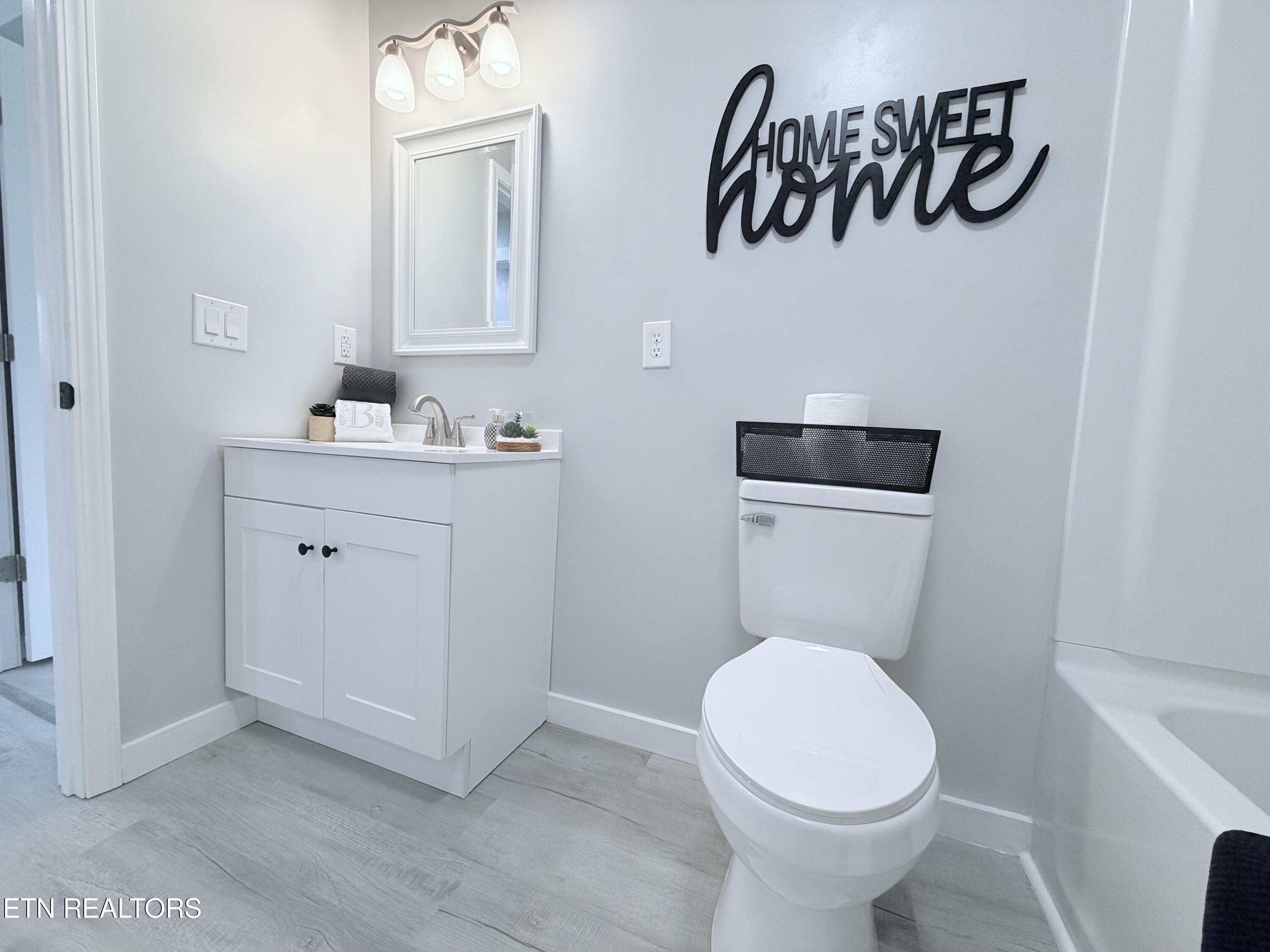 Bathroom with a white vanity and toilet beneath a black “HOME SWEET home” sign.