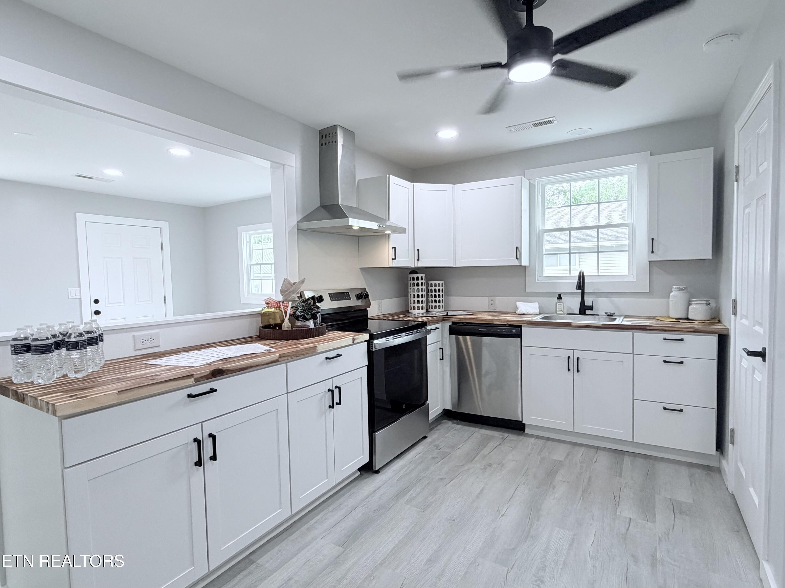 Kitchen with white cabinets, striped wood countertops, stainless steel appliances, and gray plank flooring.