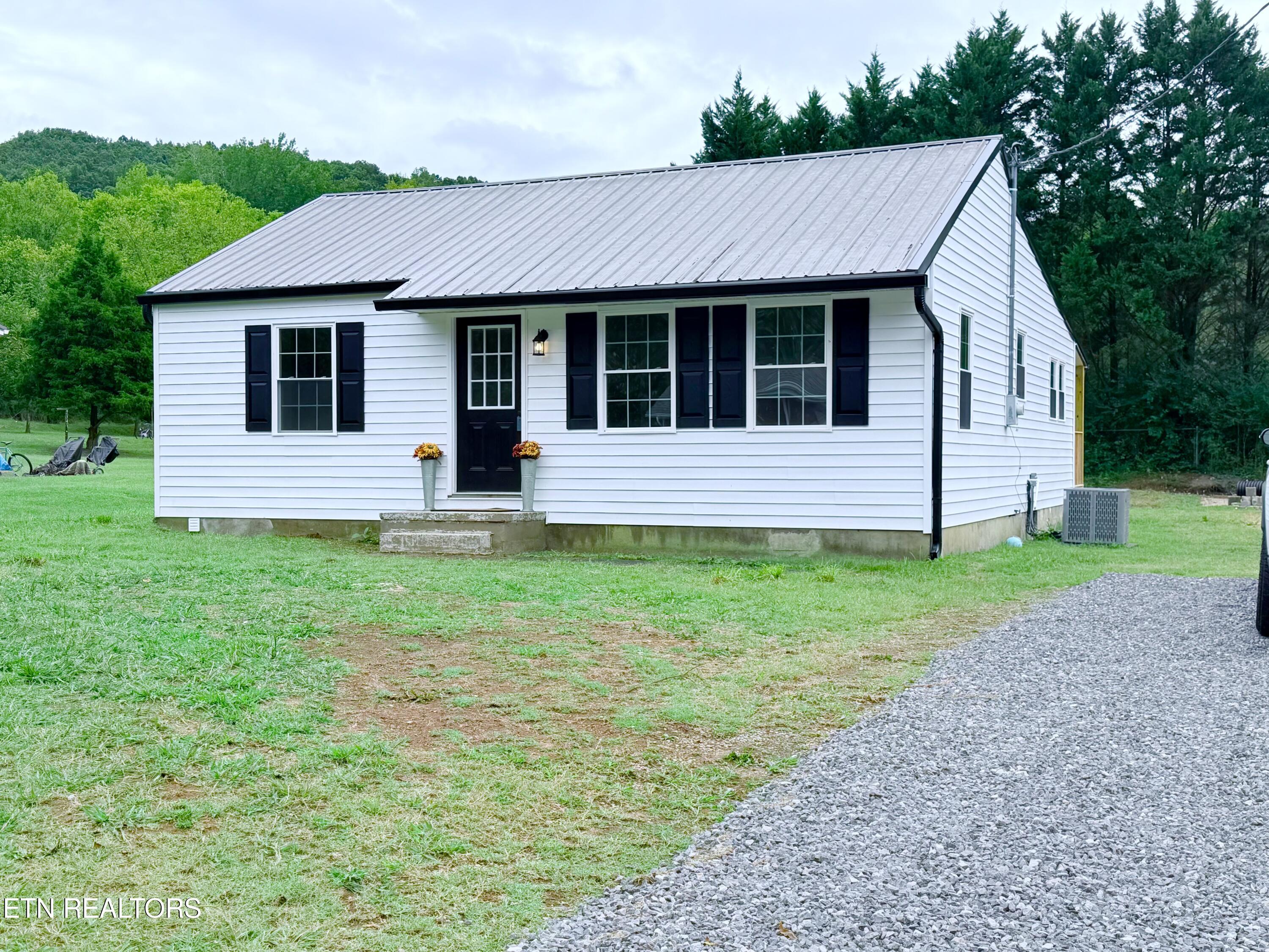 White single-story home with black shutters, a metal roof, and a gravel driveway.