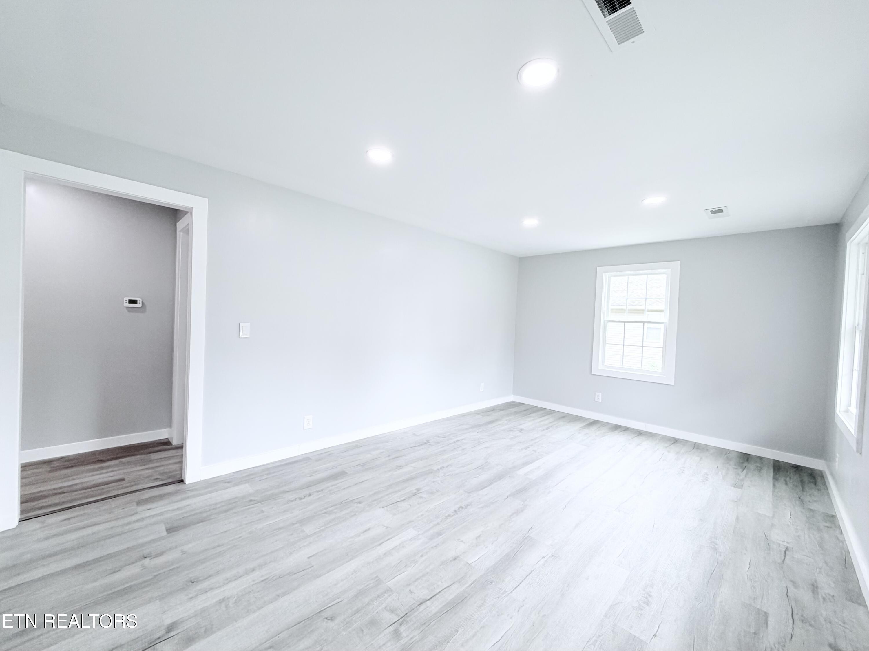 Empty room with gray plank flooring, recessed lights, and windows.
