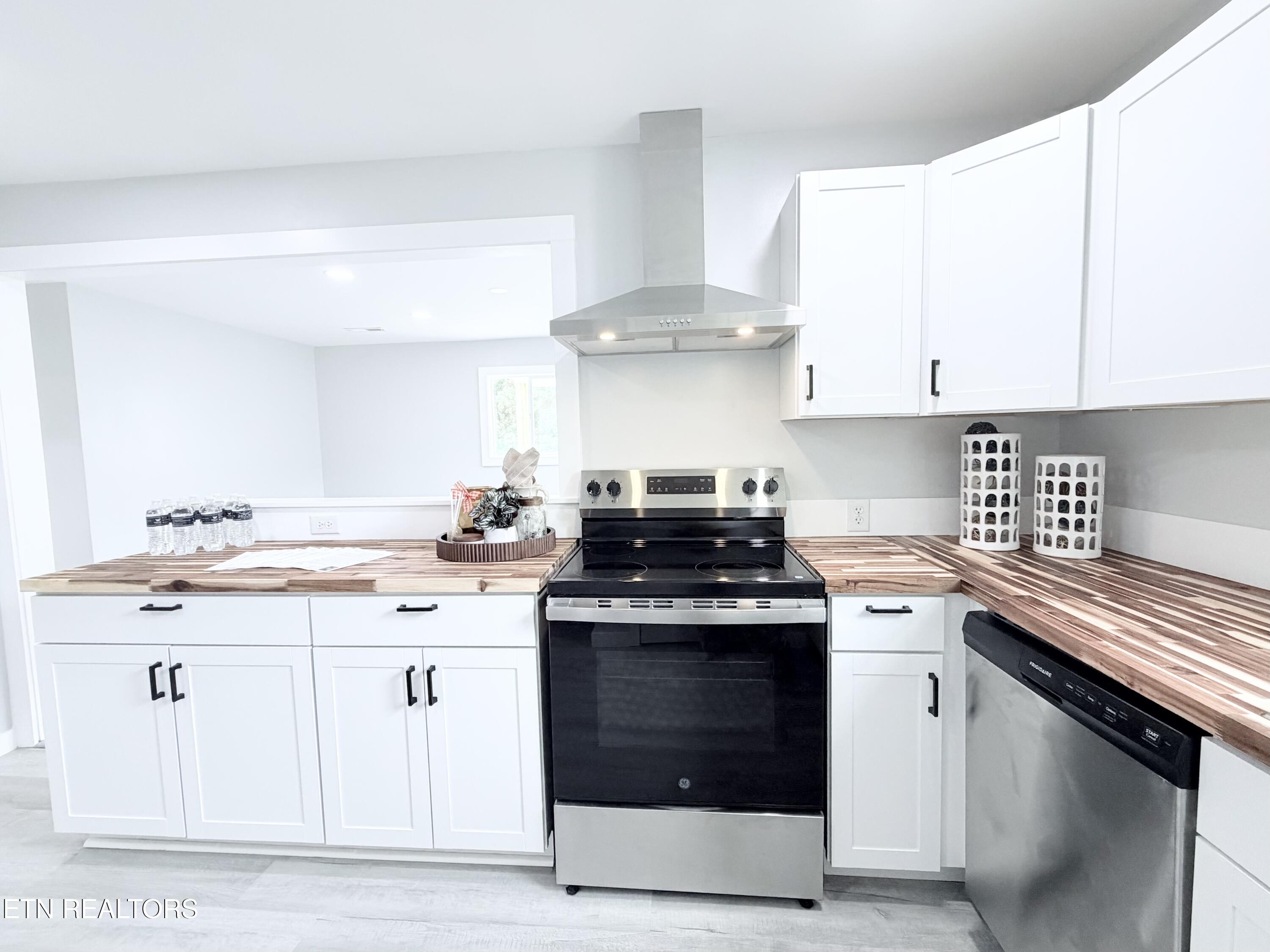 Kitchen with white shaker cabinets, striped butcher-block counters, and a black-and-stainless range.