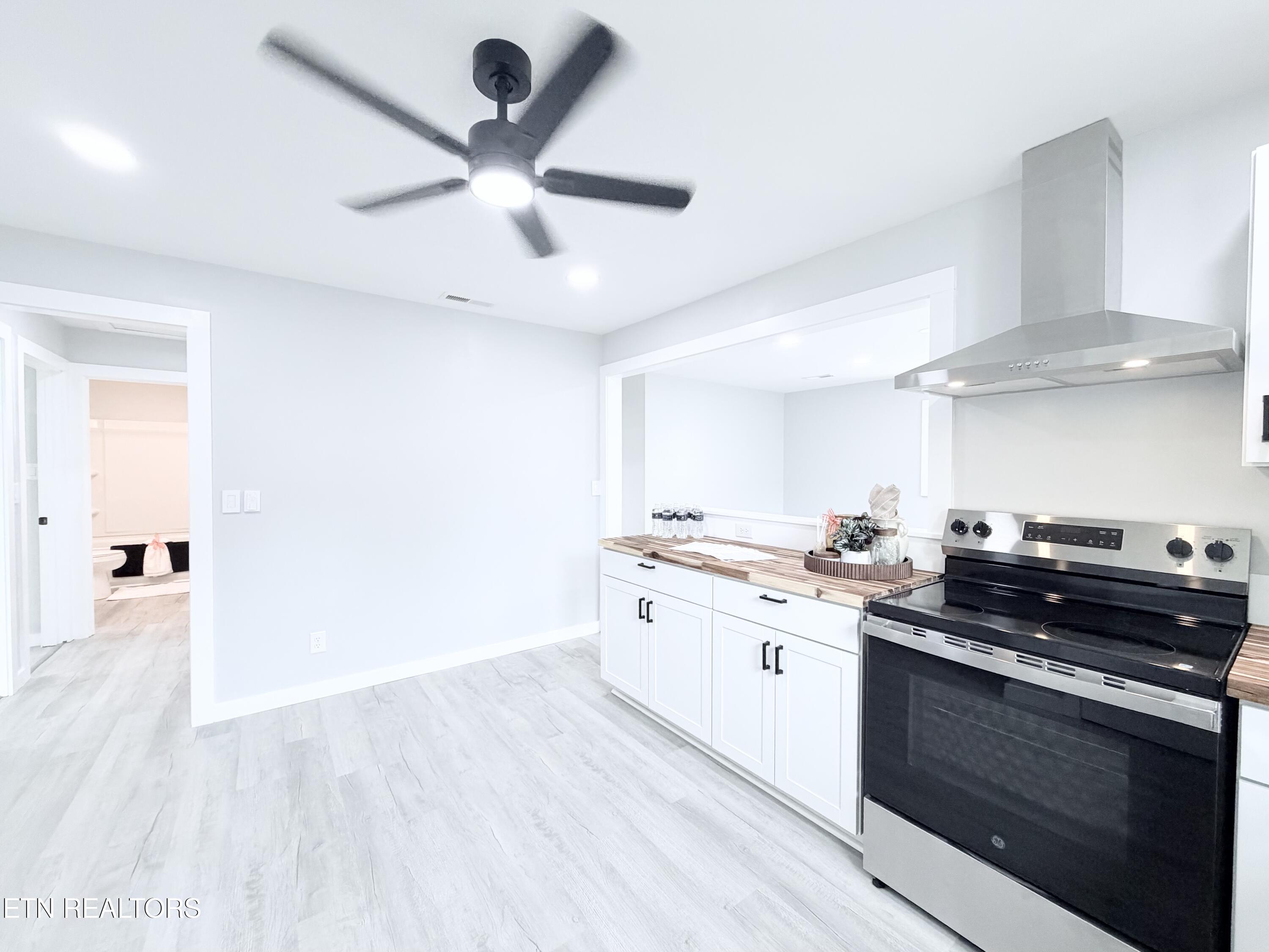 Bright white kitchen with wood countertops, stainless-steel range, and black ceiling fan.