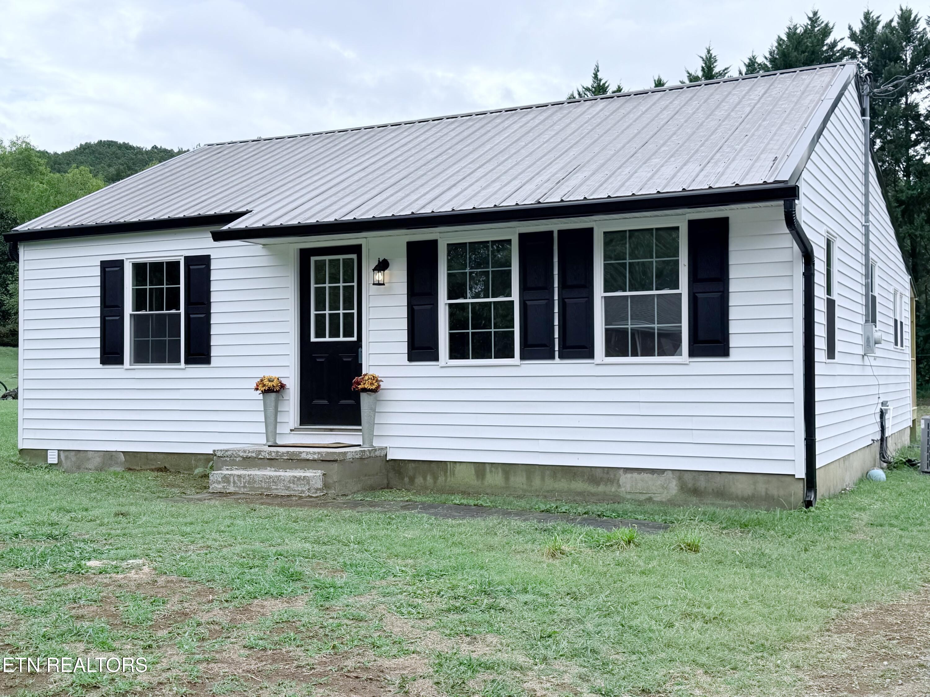 White single-story house with a metal roof, black shutters, and flower planters by the front door.