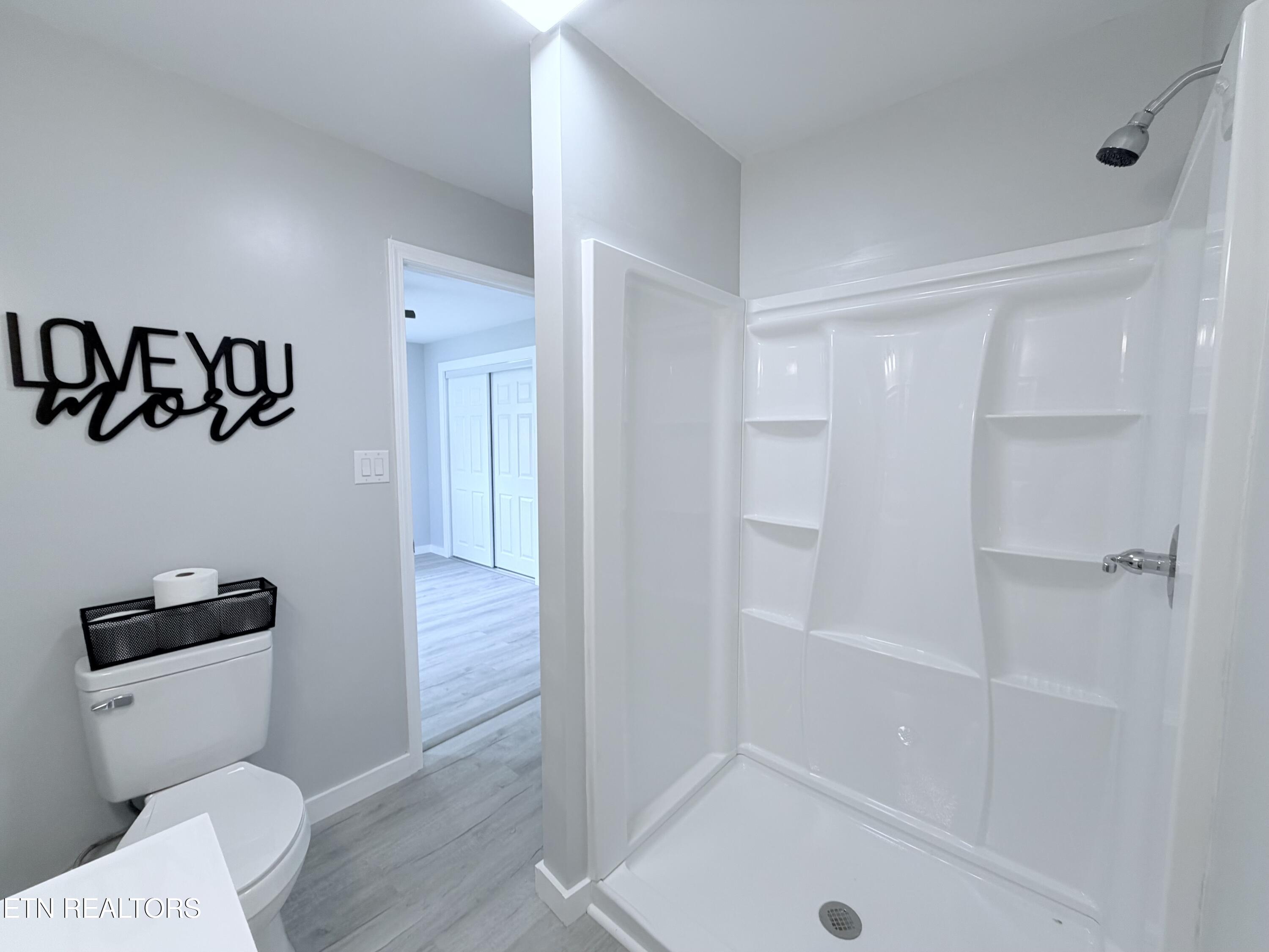 Bathroom with a white walk-in shower, built-in shelves, gray flooring, and a toilet beneath wall decor.