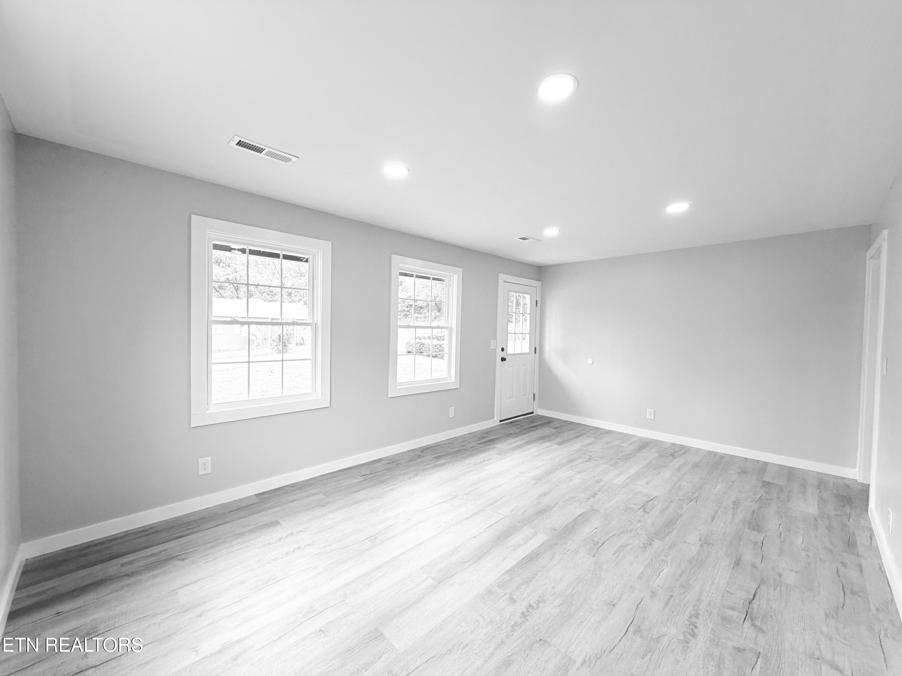 Vacant room with gray walls, plank flooring, two windows, and a glazed exterior door.