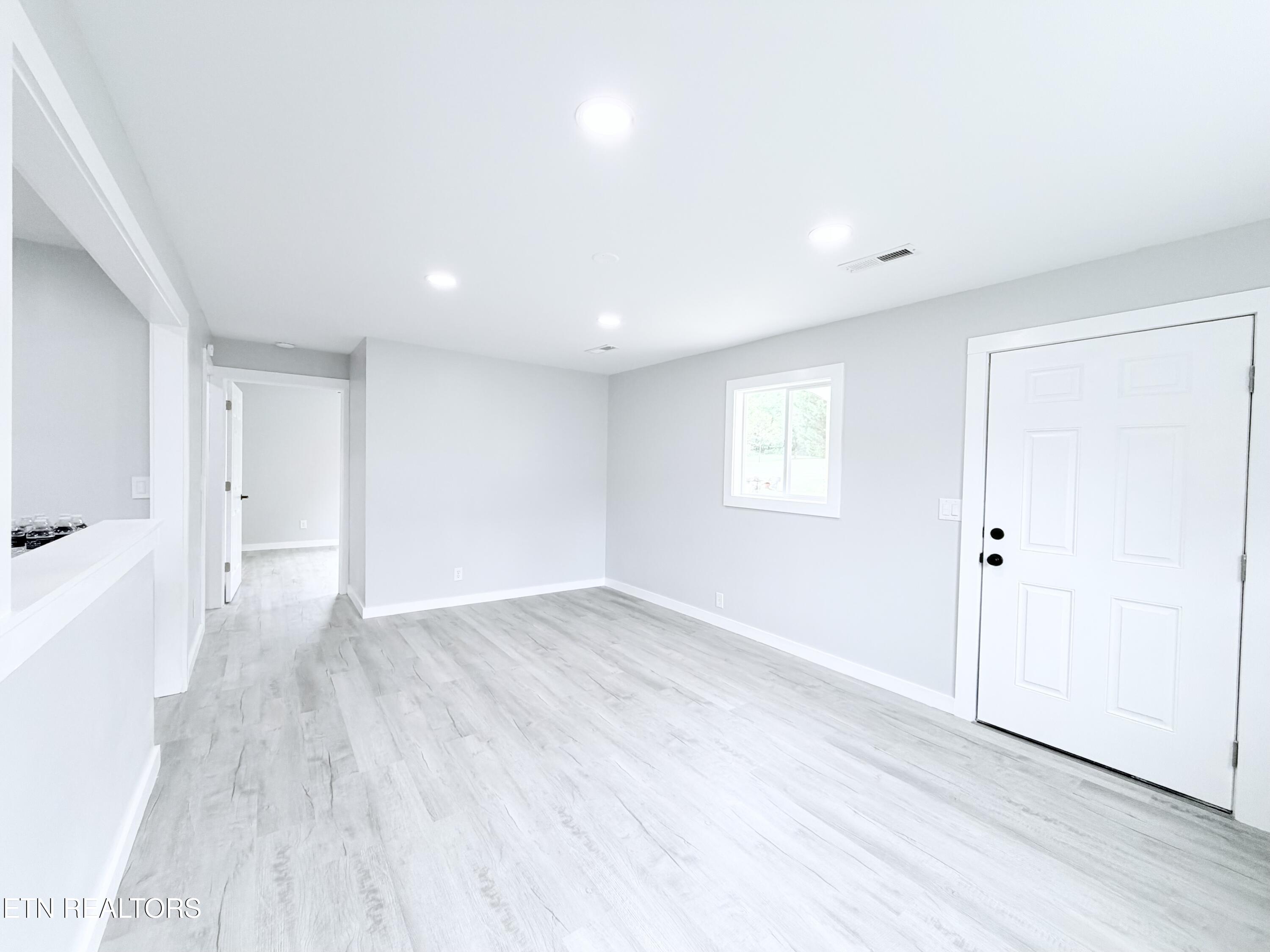 Empty interior room with pale plank flooring, recessed lights, a window, and a white entry door.