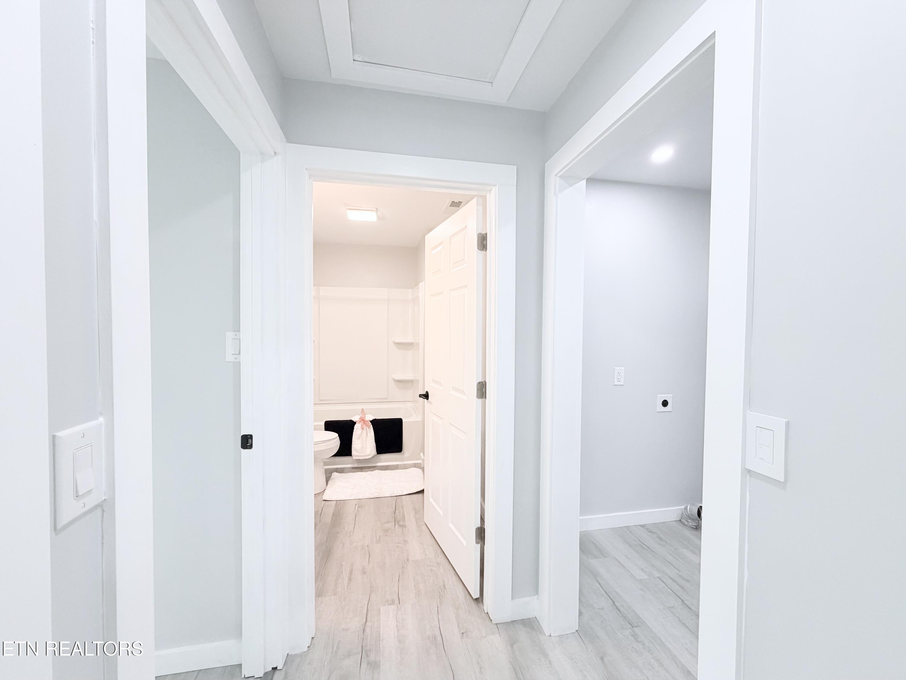 Hallway leading to a bathroom with a tub and toilet, beside an open doorway to an empty room.