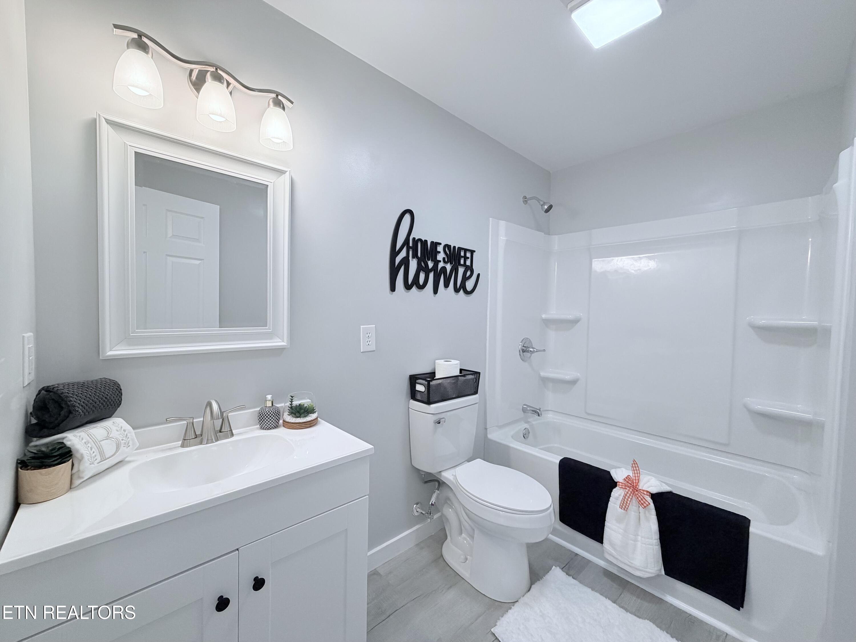 Bathroom with a white vanity, toilet, and tub-shower combination with black-and-white towels.