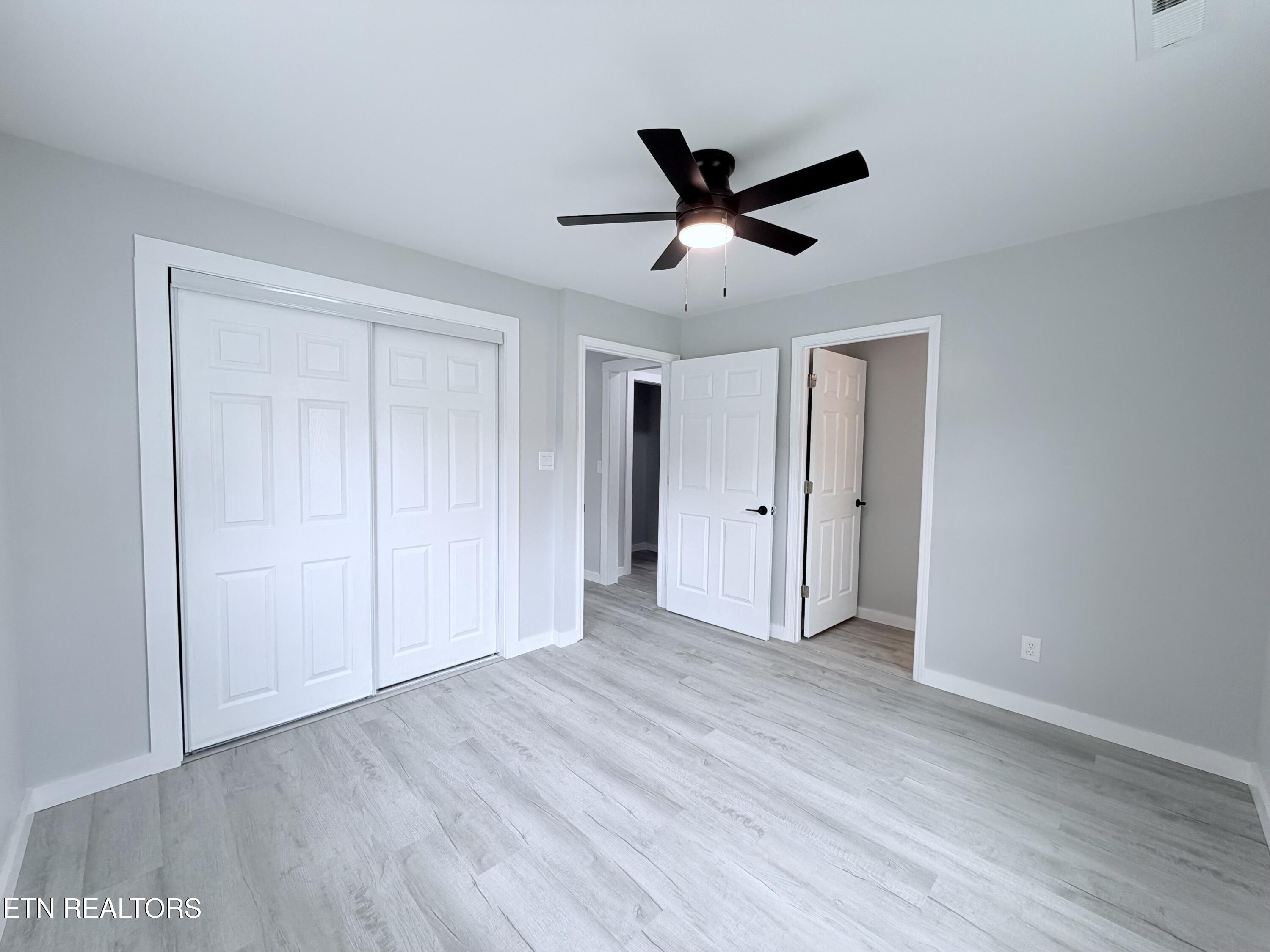 Empty bedroom with sliding closet doors, light wood-look flooring, and a black ceiling fan.