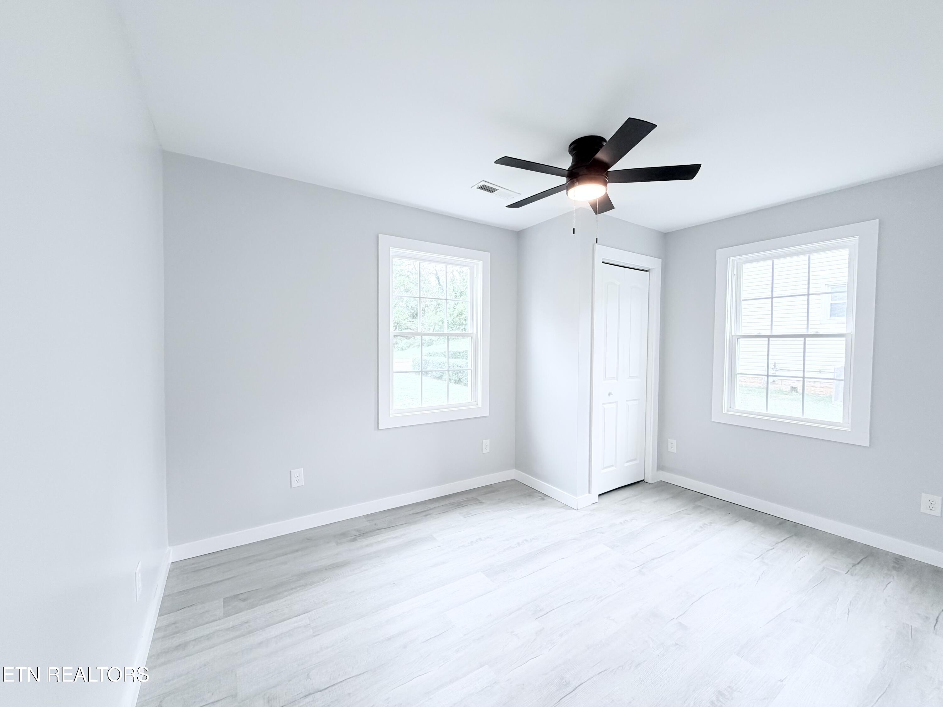 Empty room with pale flooring, two windows, a white closet door, and a black ceiling fan.