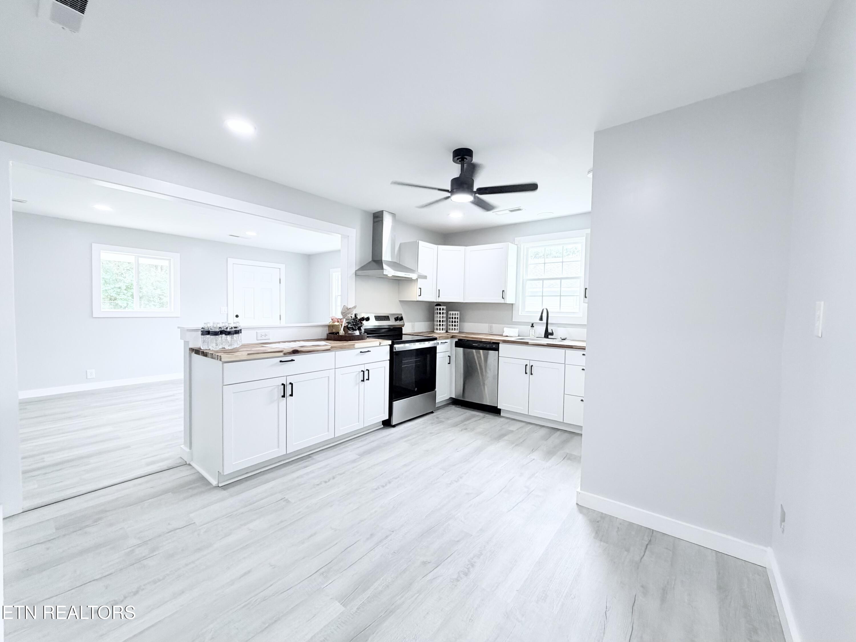 Bright kitchen with white cabinets, wood countertops, stainless steel appliances, and an open adjoining room.