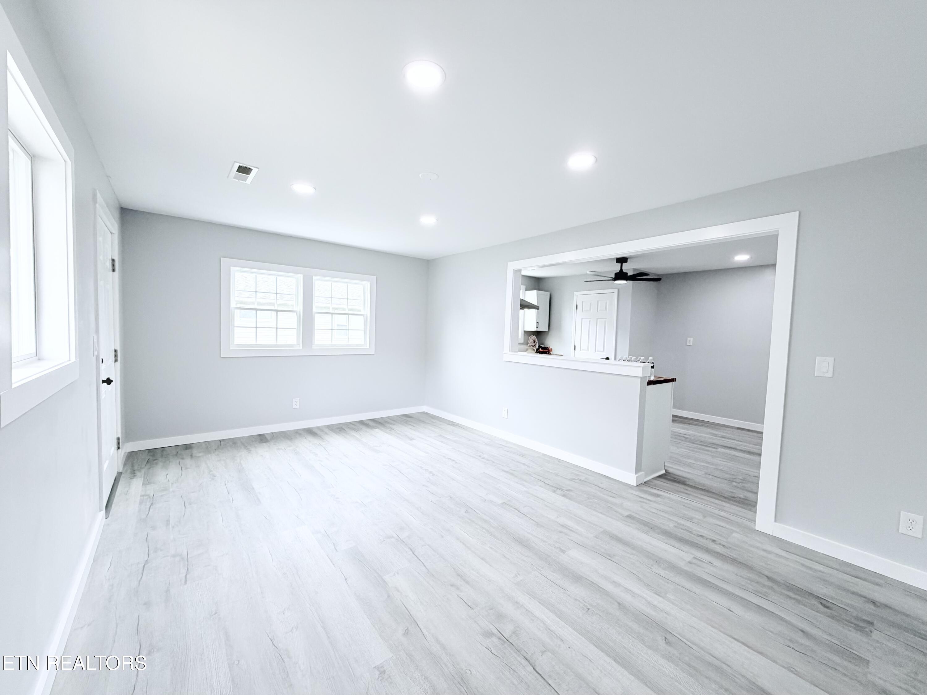 Empty living area with light wood-look floors and a wide opening to the kitchen.