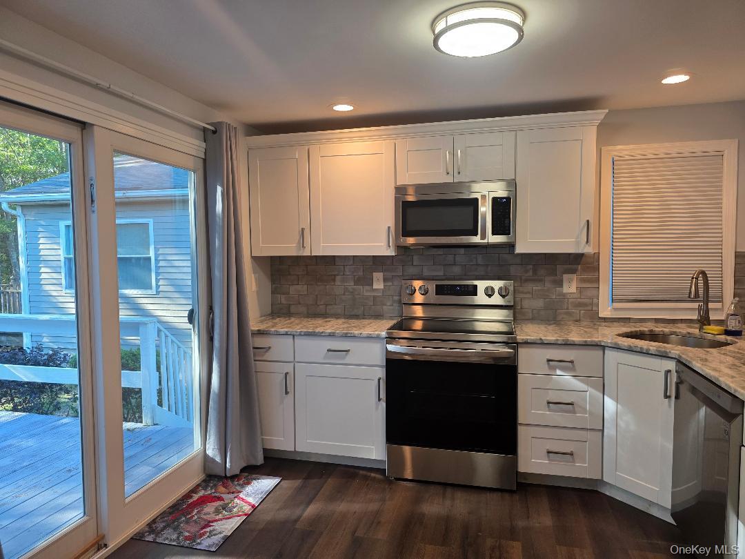 Kitchen with white shaker cabinets, stainless steel appliances, and sliding glass doors to a deck.