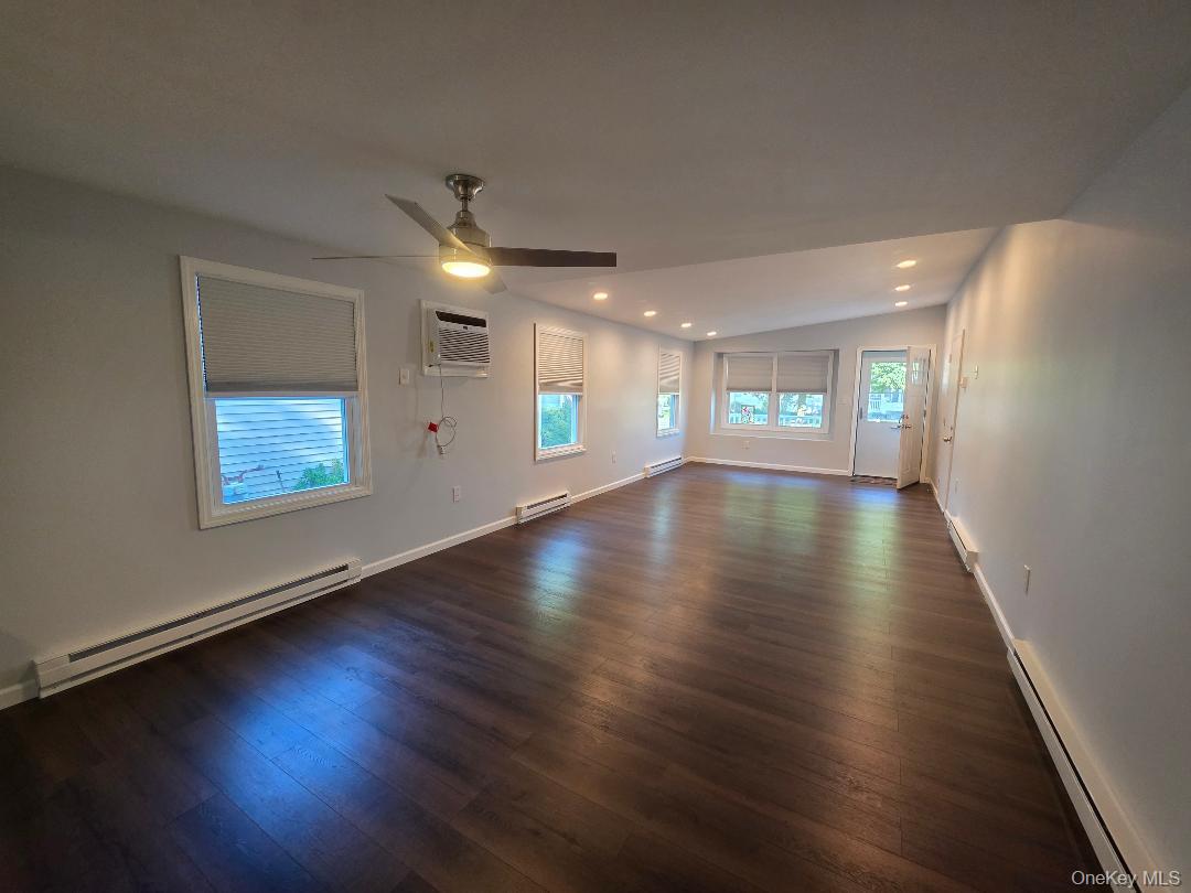 Vacant living room with dark wood floors, multiple windows, a ceiling fan, and a window air conditioner.
