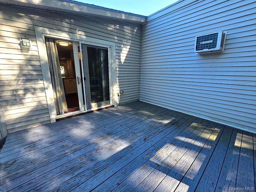 Weathered wooden deck beside gray siding, with a sliding glass door and window air conditioner.