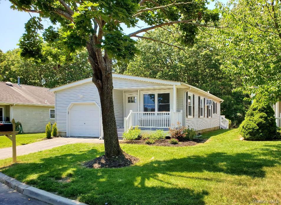 Single-story home with attached garage and covered porch beneath a large shade tree.