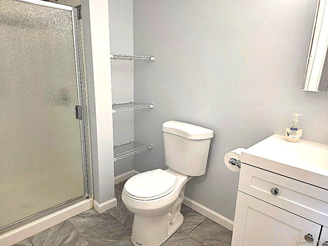 Bathroom with a frosted-glass shower, wire shelves, white toilet, and gray tile floor.